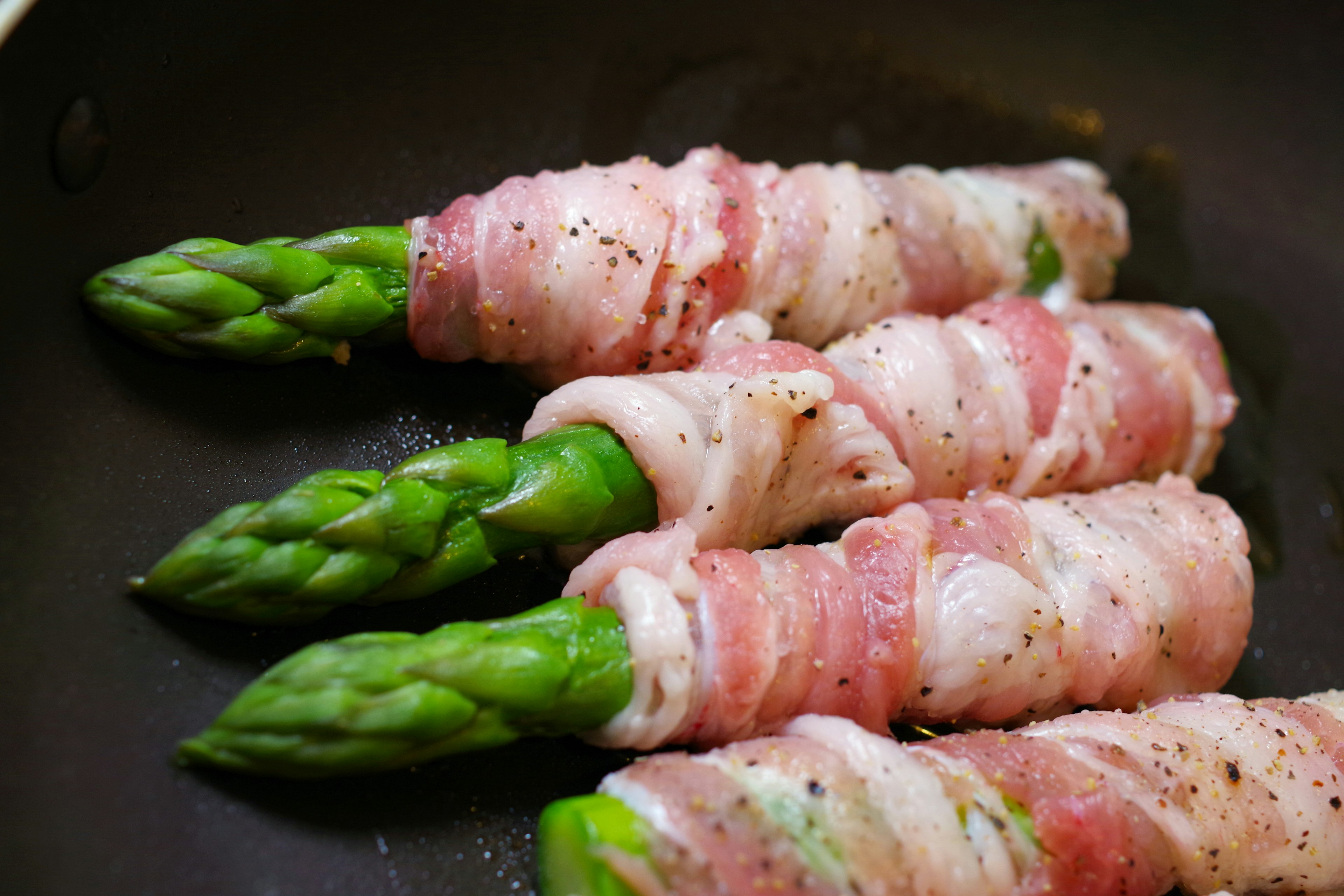 Asparagus wrapped in bacon arranged in a frying pan