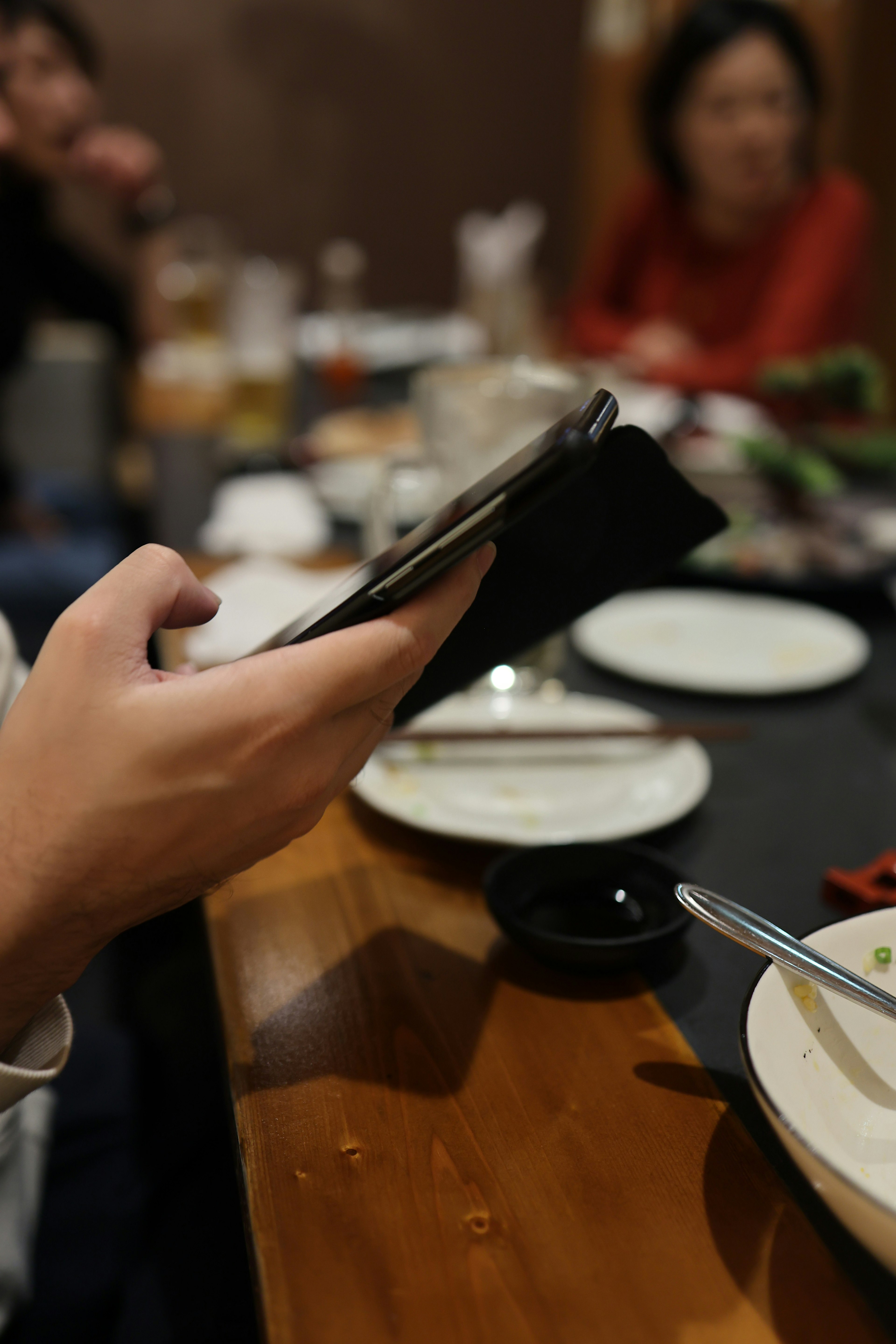 A hand holding a smartphone at a dining table with plates and drinks