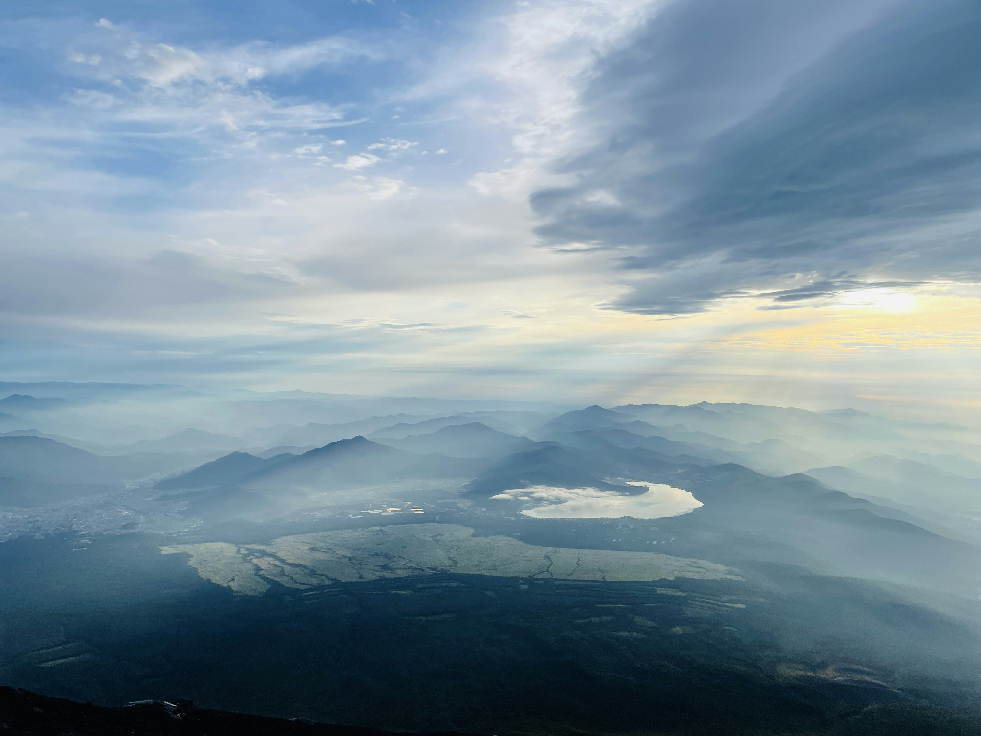 Paesaggio maestoso dalla cima di una montagna con montagne nebbiose e cielo blu con un lago visibile al centro