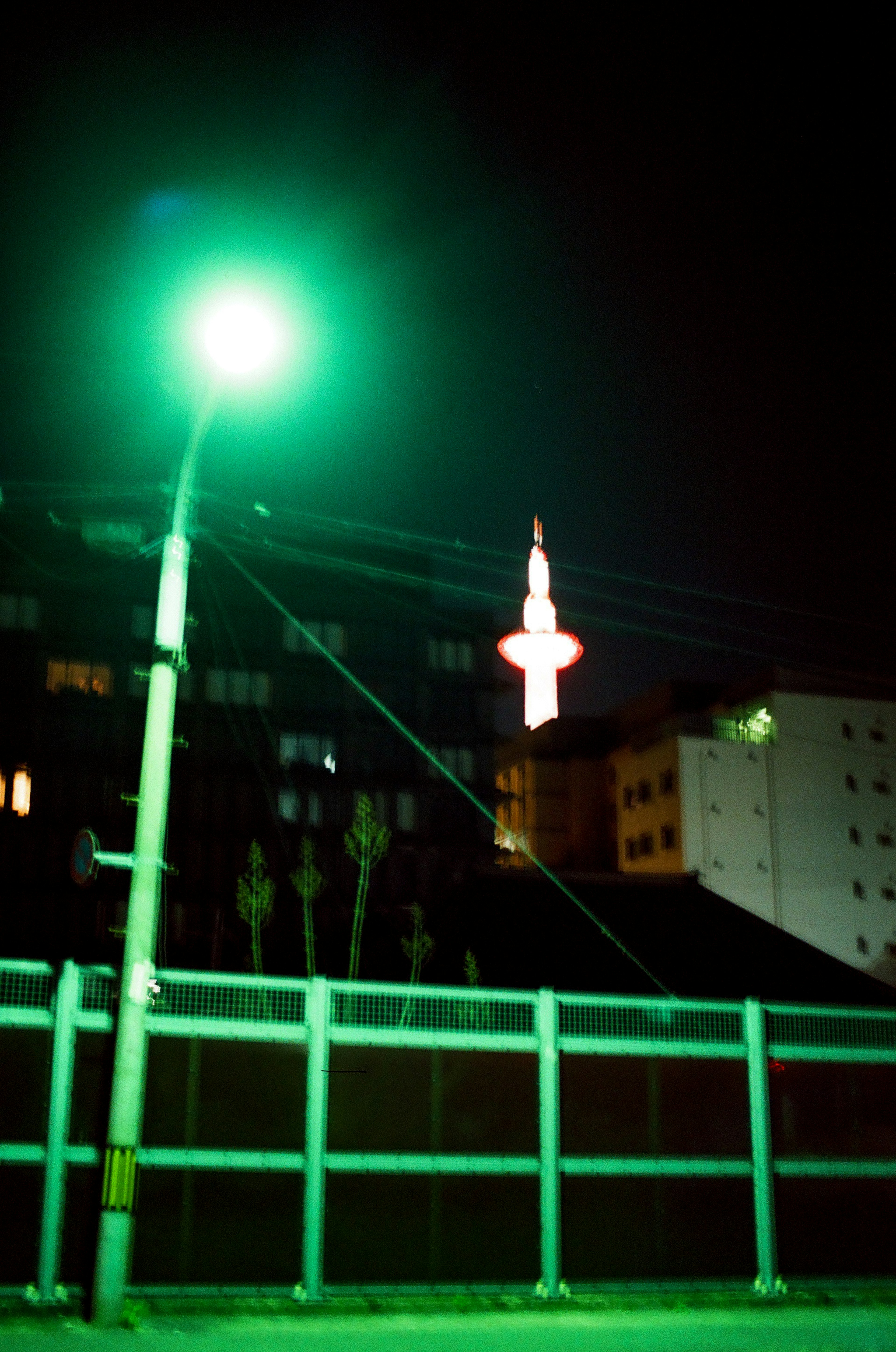 Escena nocturna con una farola verde y una torre al fondo