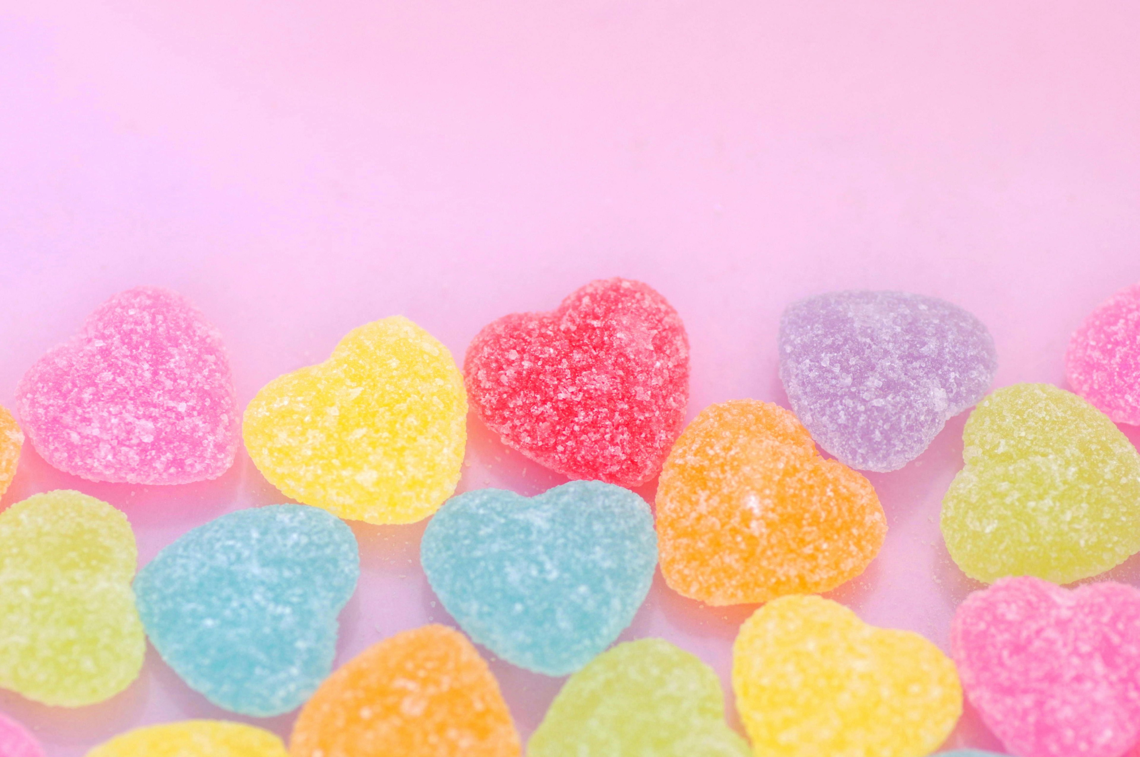 Colorful heart-shaped gummy candies arranged on a pink background