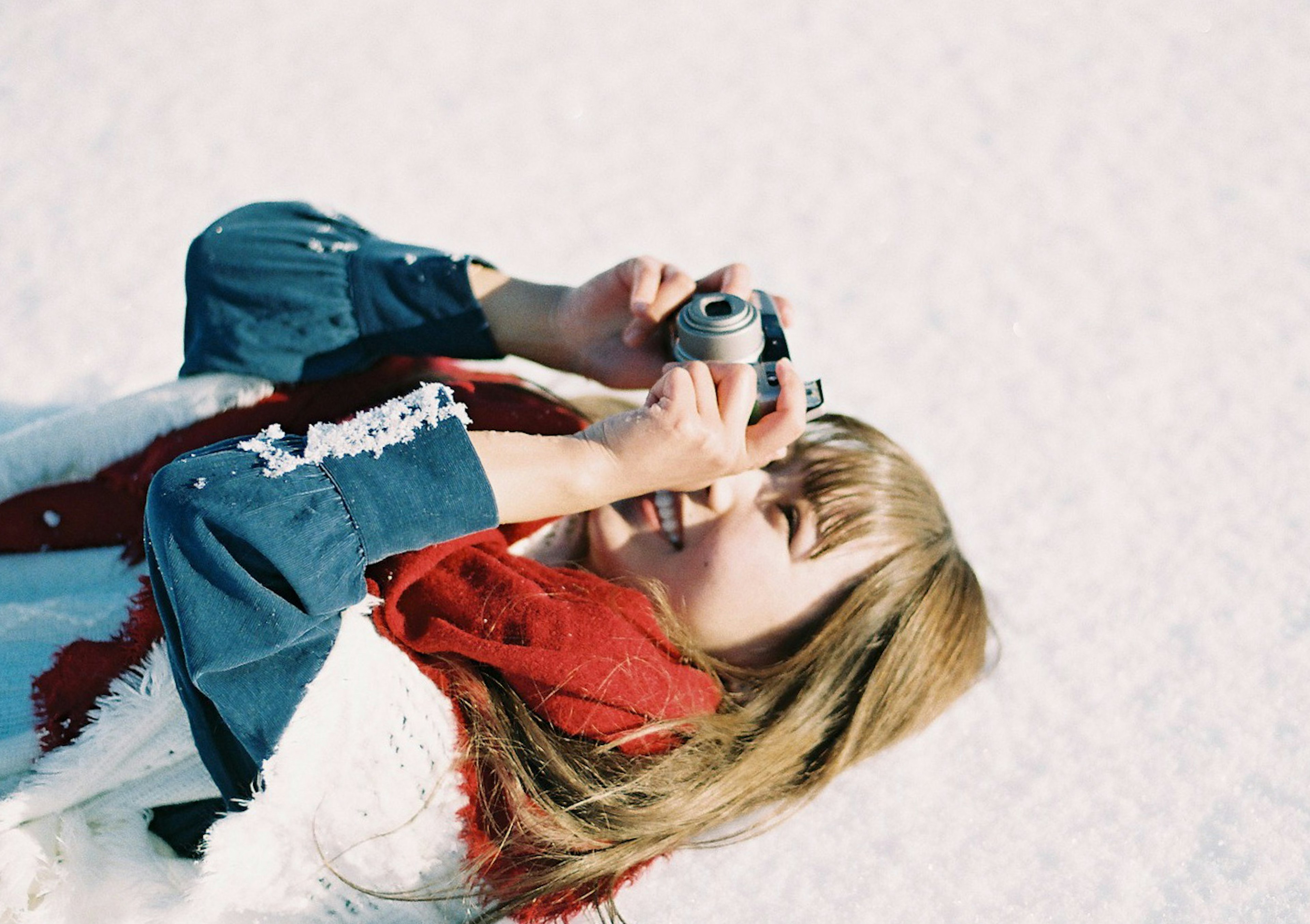 Woman taking a photo with a camera wearing a red scarf and winter attire