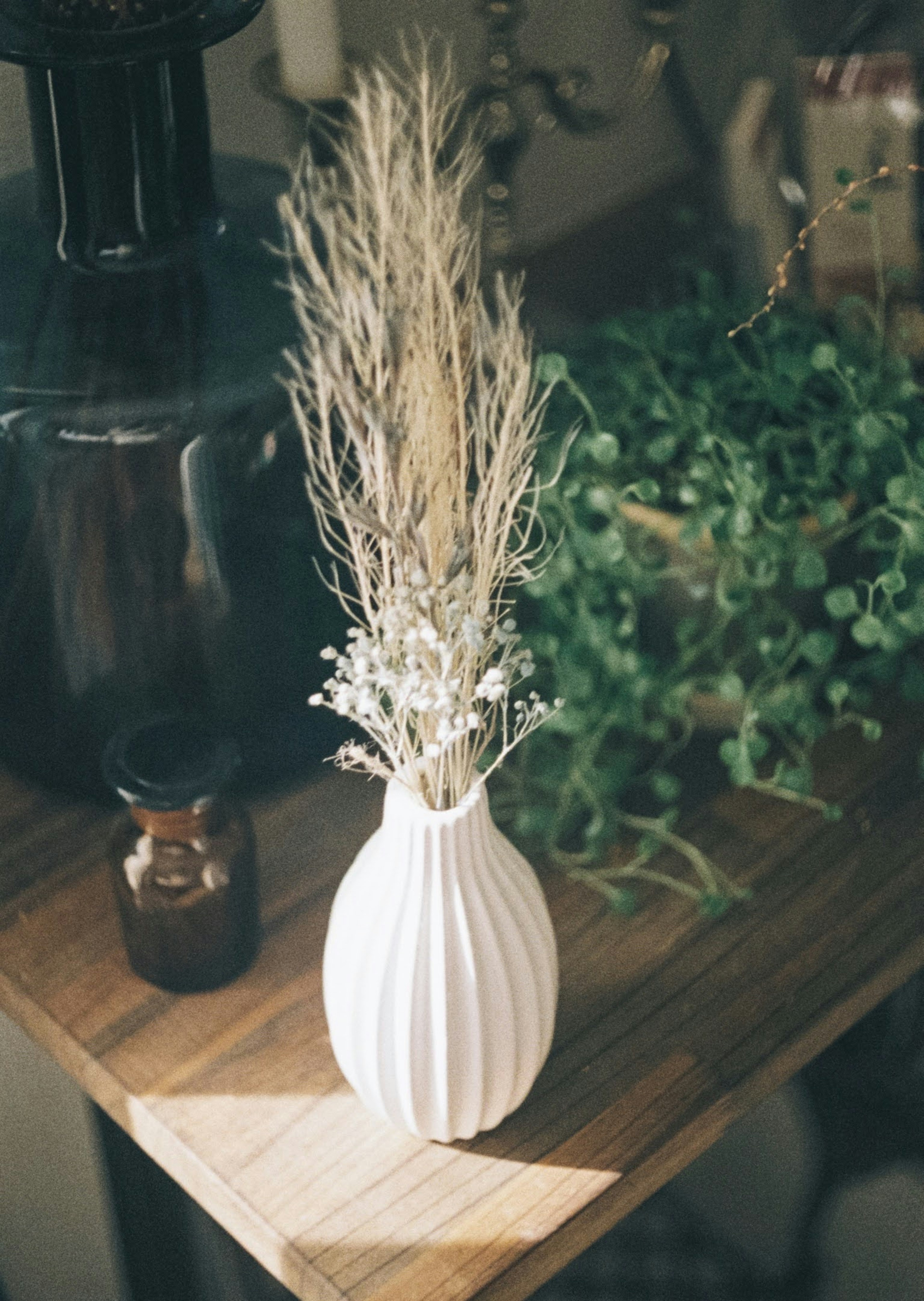 Eine weiße Vase mit getrocknetem Gras und kleinen Blumen auf einem Holztisch