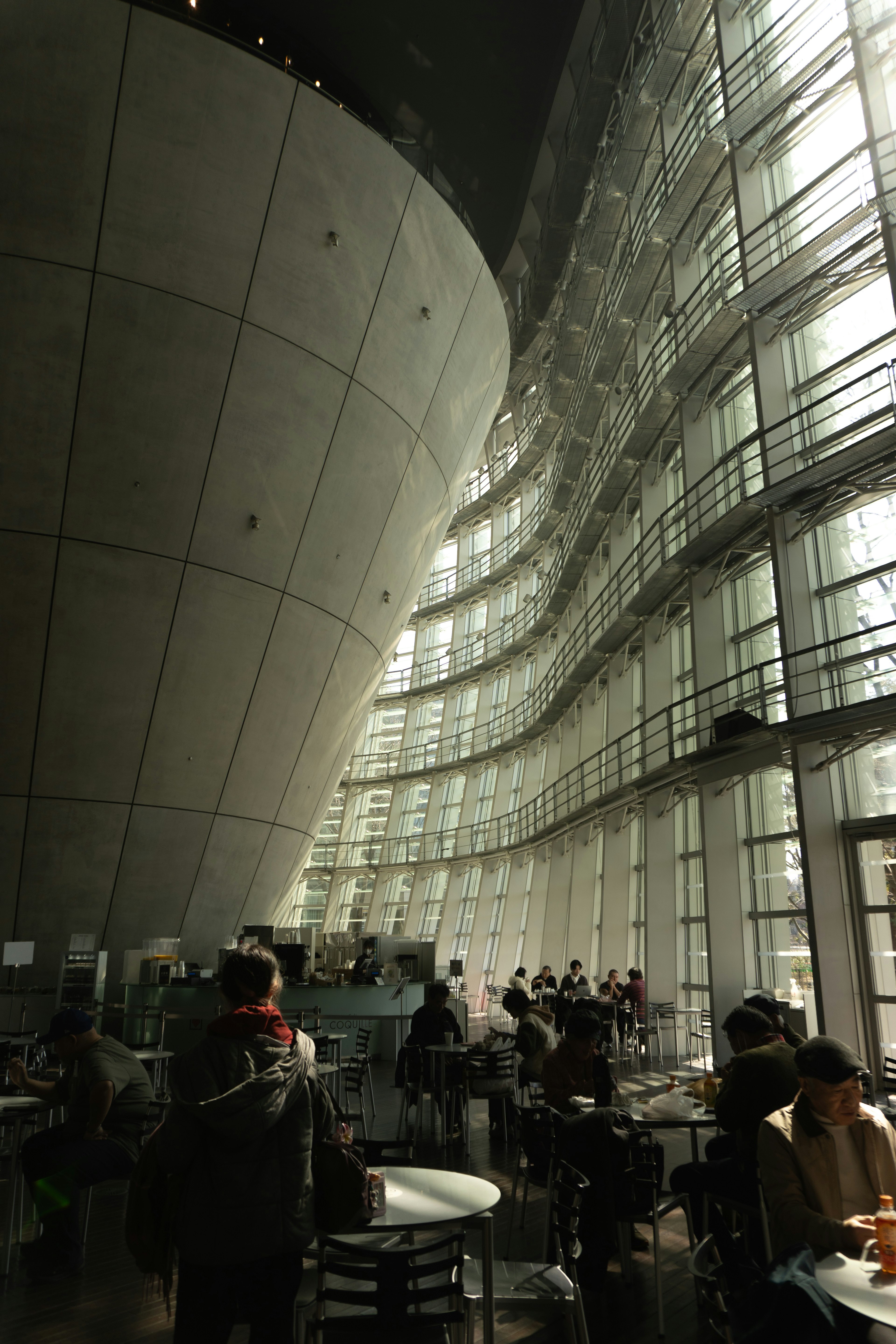 Interior de un espacio arquitectónico moderno con paredes de vidrio curvadas y una estructura circular en un café