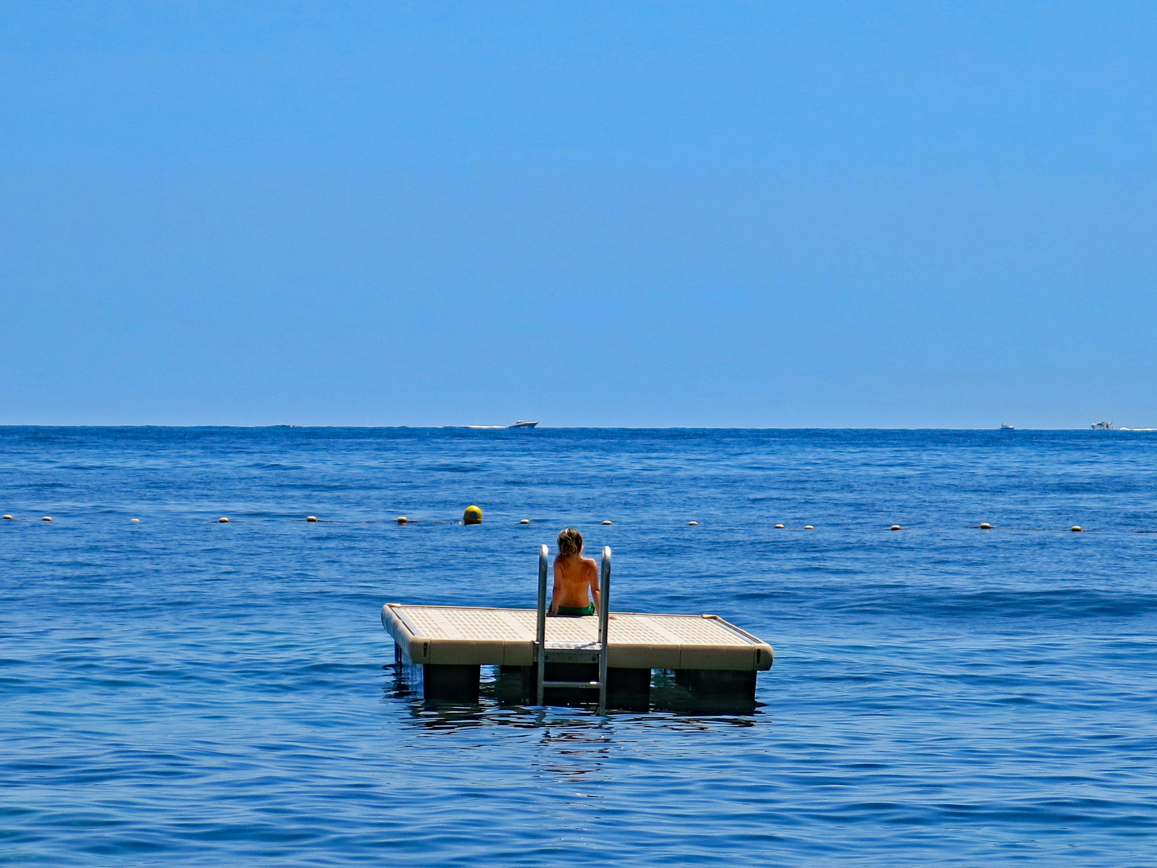 Eine Person sitzt auf einem schwimmenden Dock im blauen Ozean