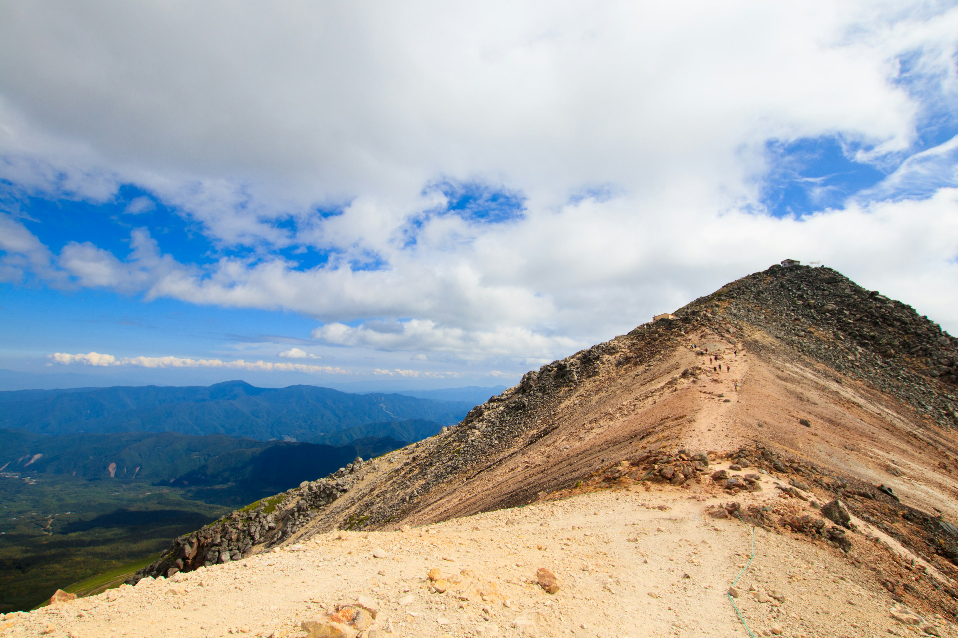 Paisaje de cumbre montañosa con cielo azul y nubes blancas que presenta un sendero marrón