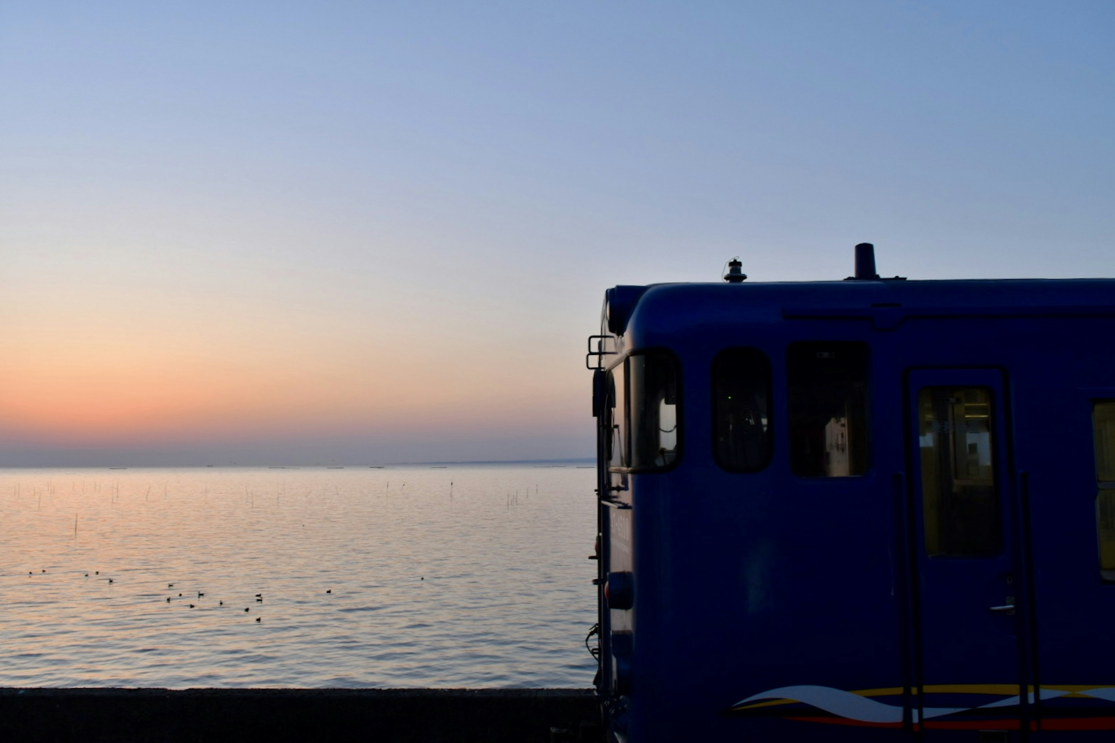 Blauer Zug vor einem Sonnenuntergang über dem Meer