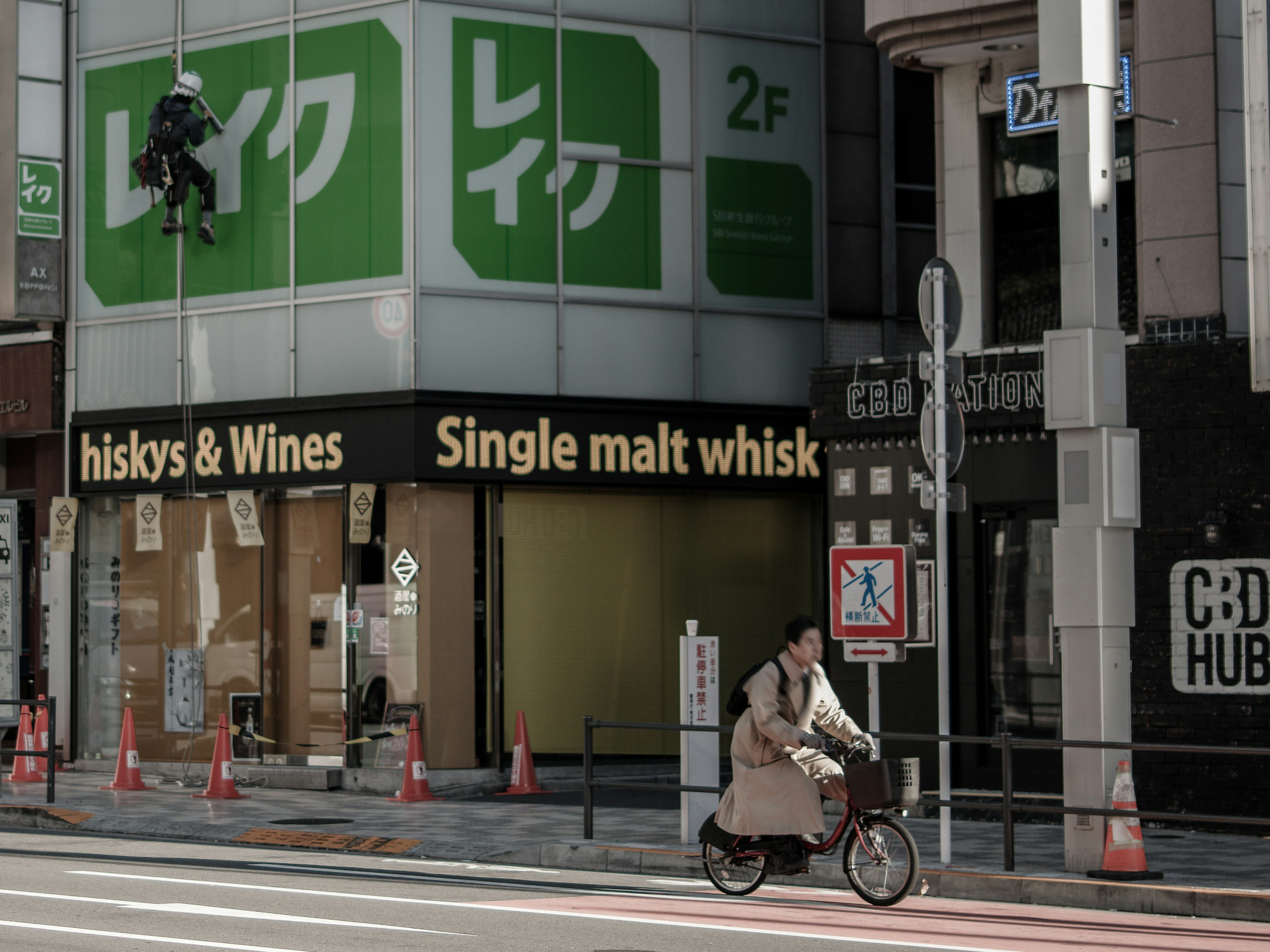 A commercial scene with a worker climbing a building and a cyclist passing by