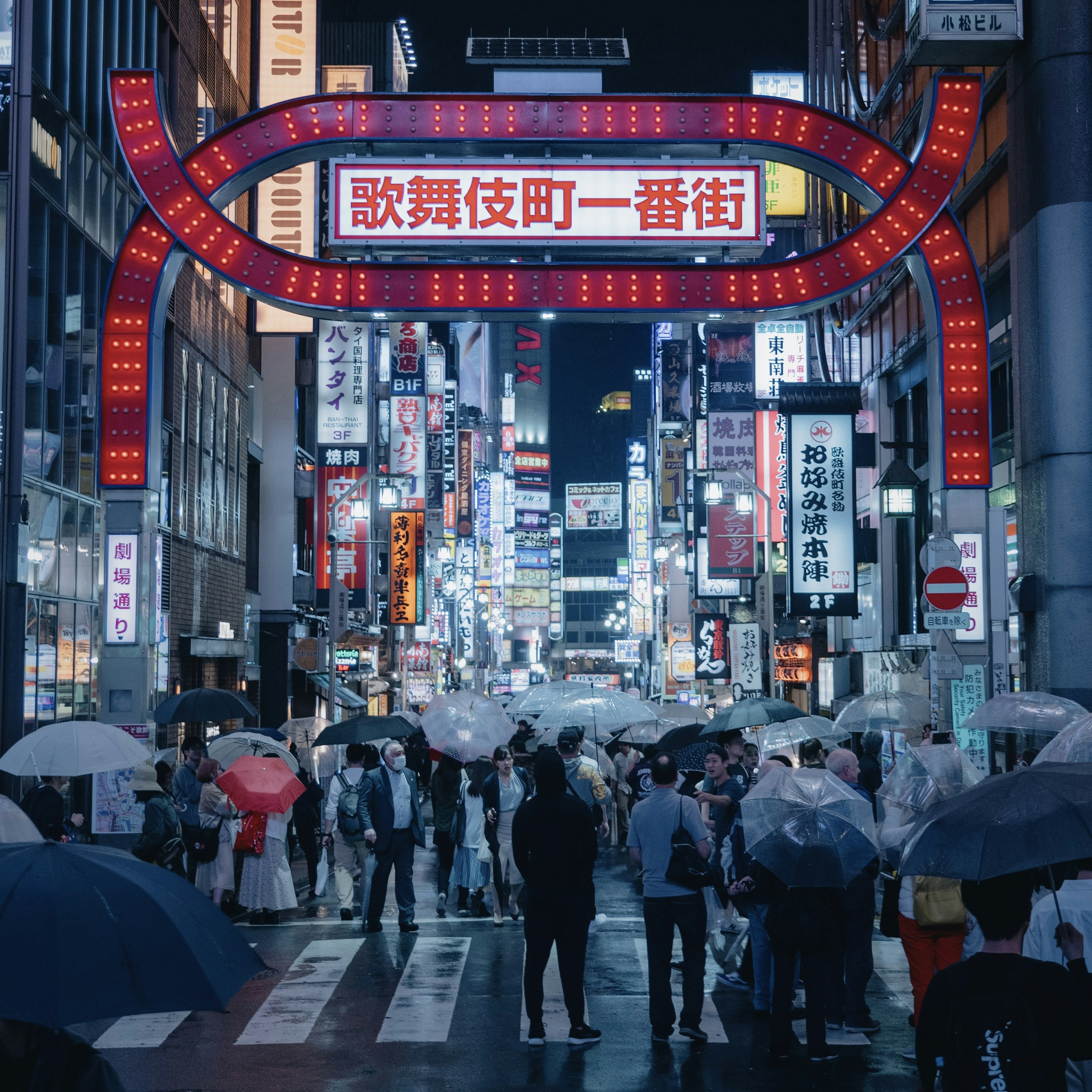 Des gens avec des parapluies dans une rue animée la nuit avec des enseignes au néon