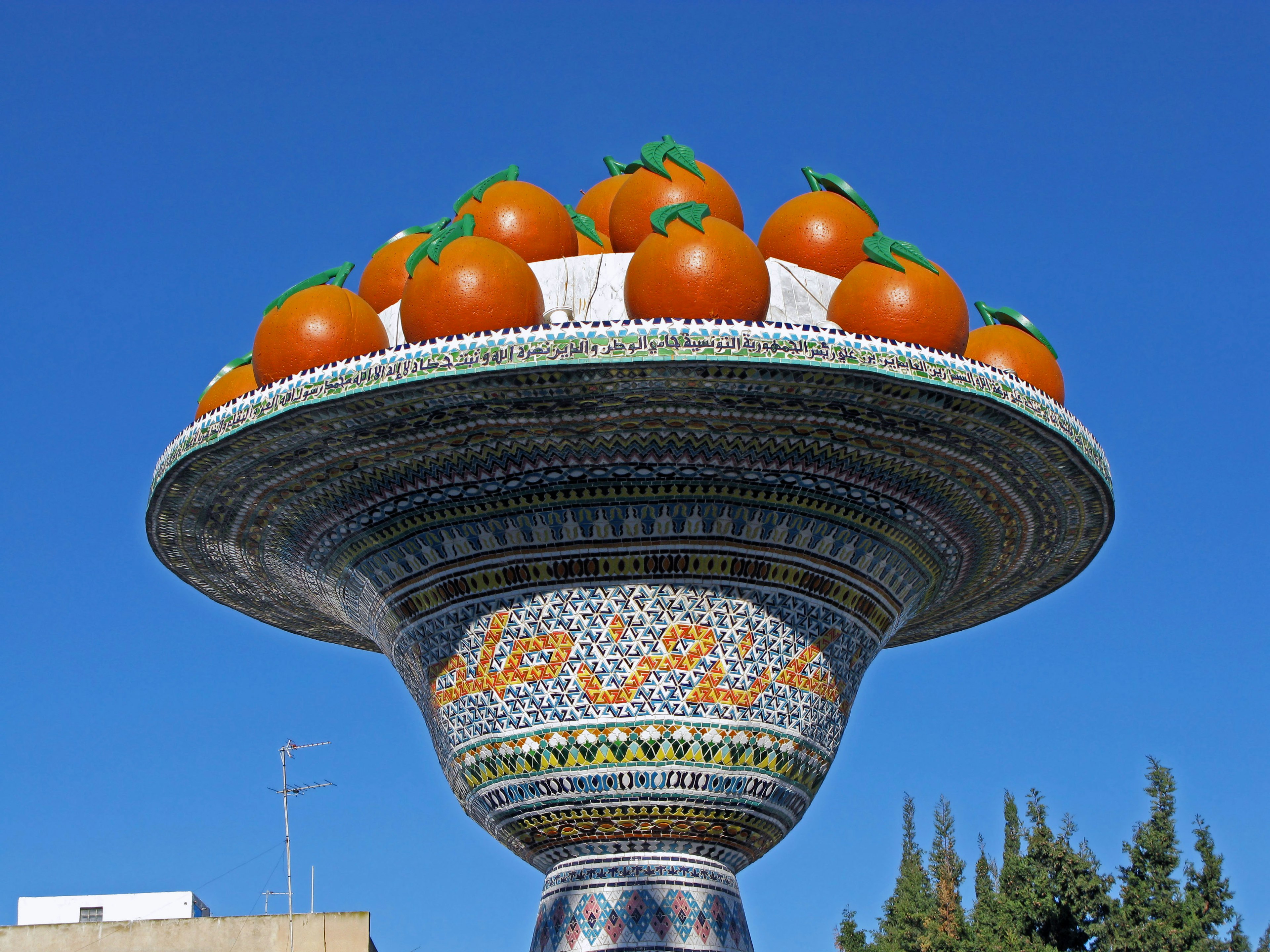 Fuente decorativa con tomates naranjas exhibidos bajo un cielo azul