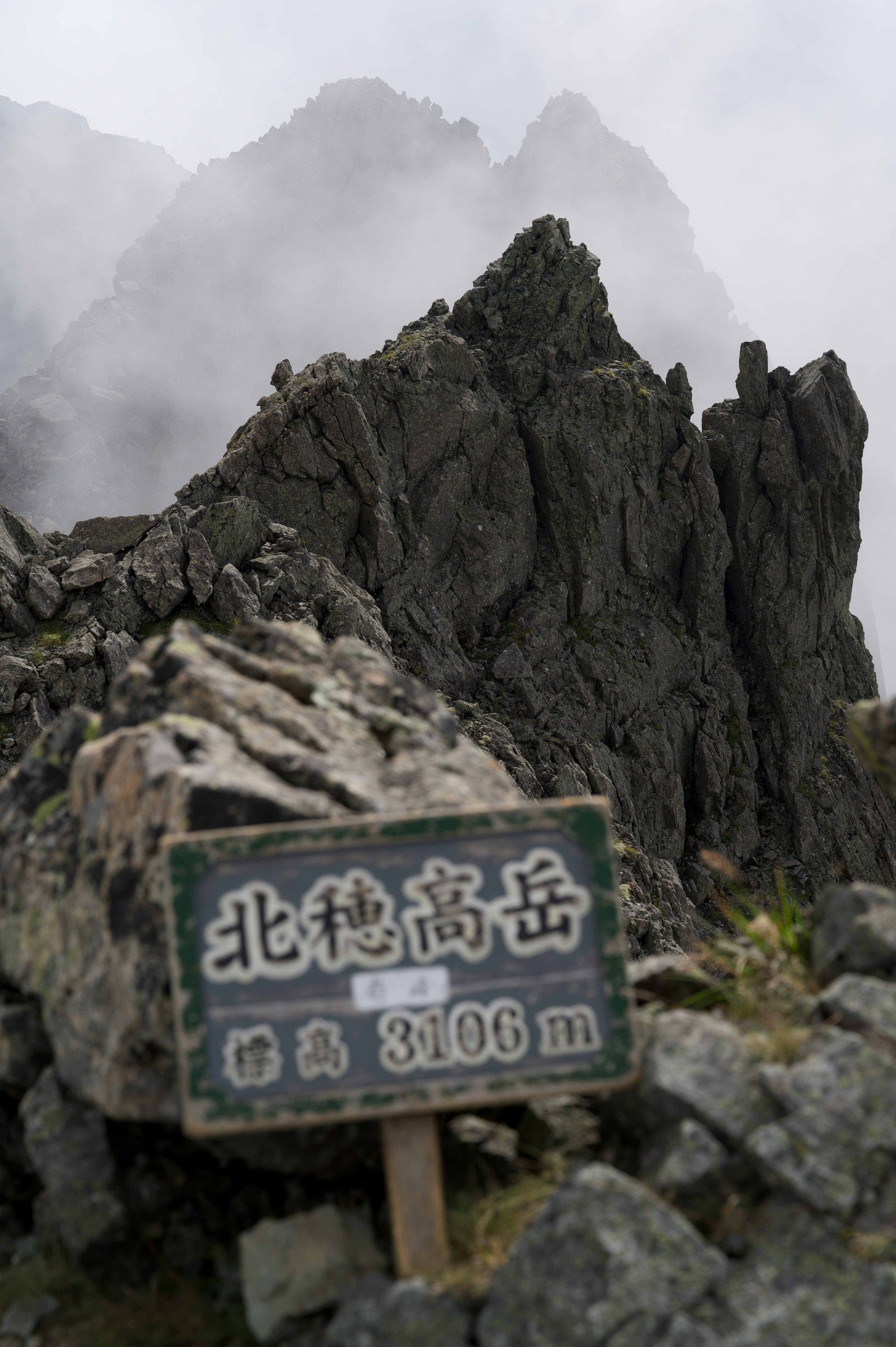 霧の中にそびえる北穂高岳の標識と岩