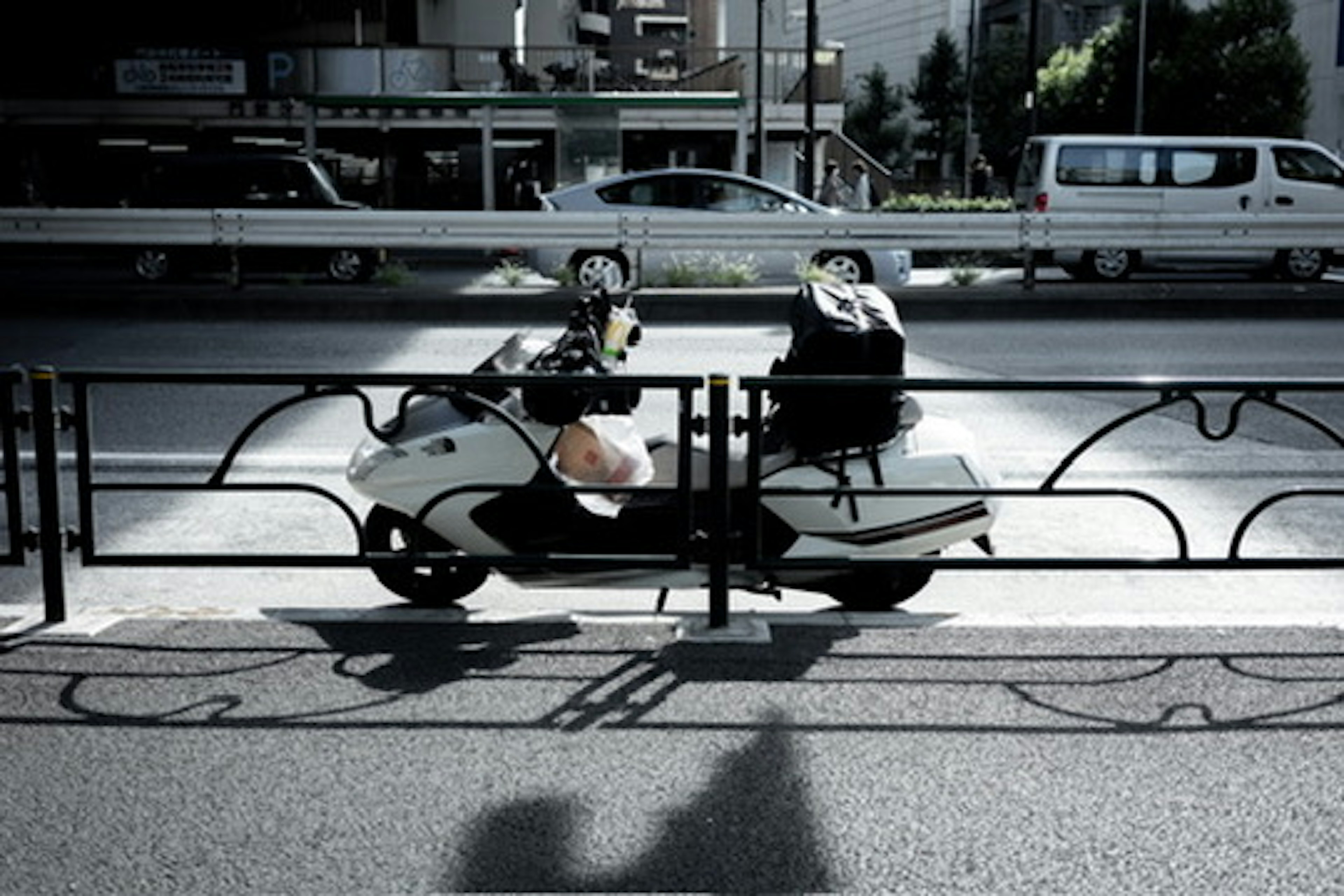 A white scooter parked in front of a railing on a city street