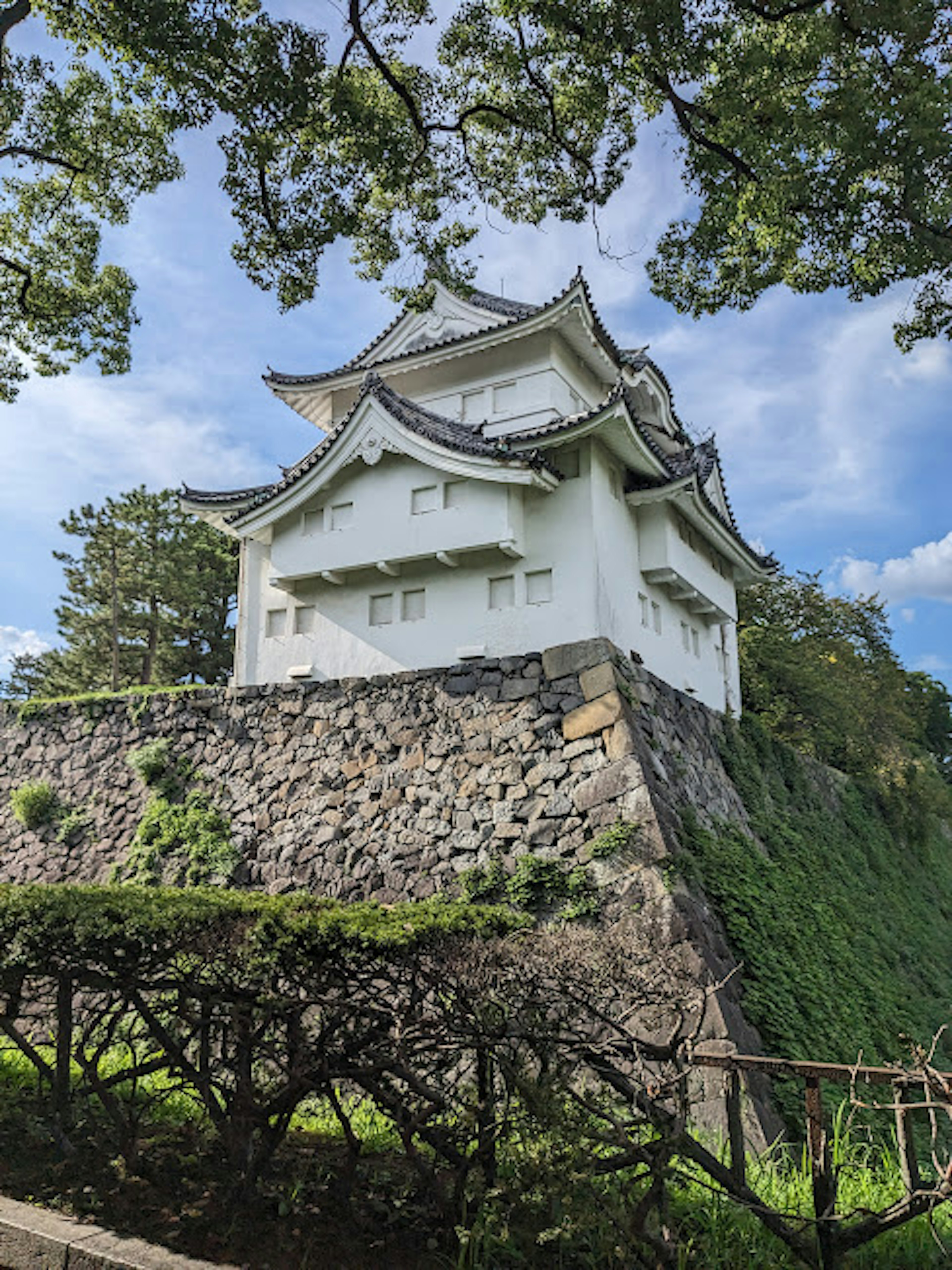 白い城が緑の木々の中に立つ石の壁の上にある