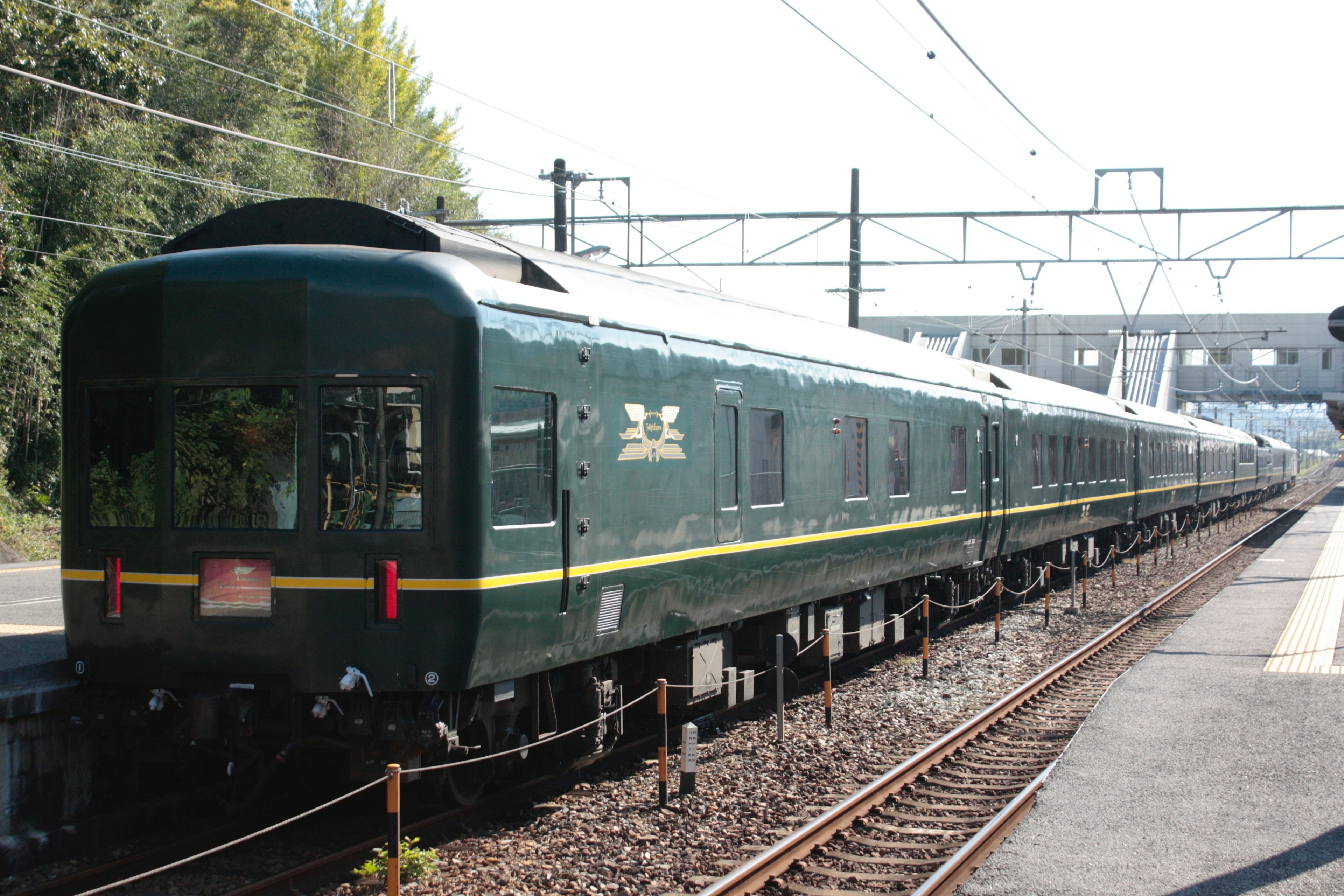 一列綠色火車停在車站，周圍有樹木