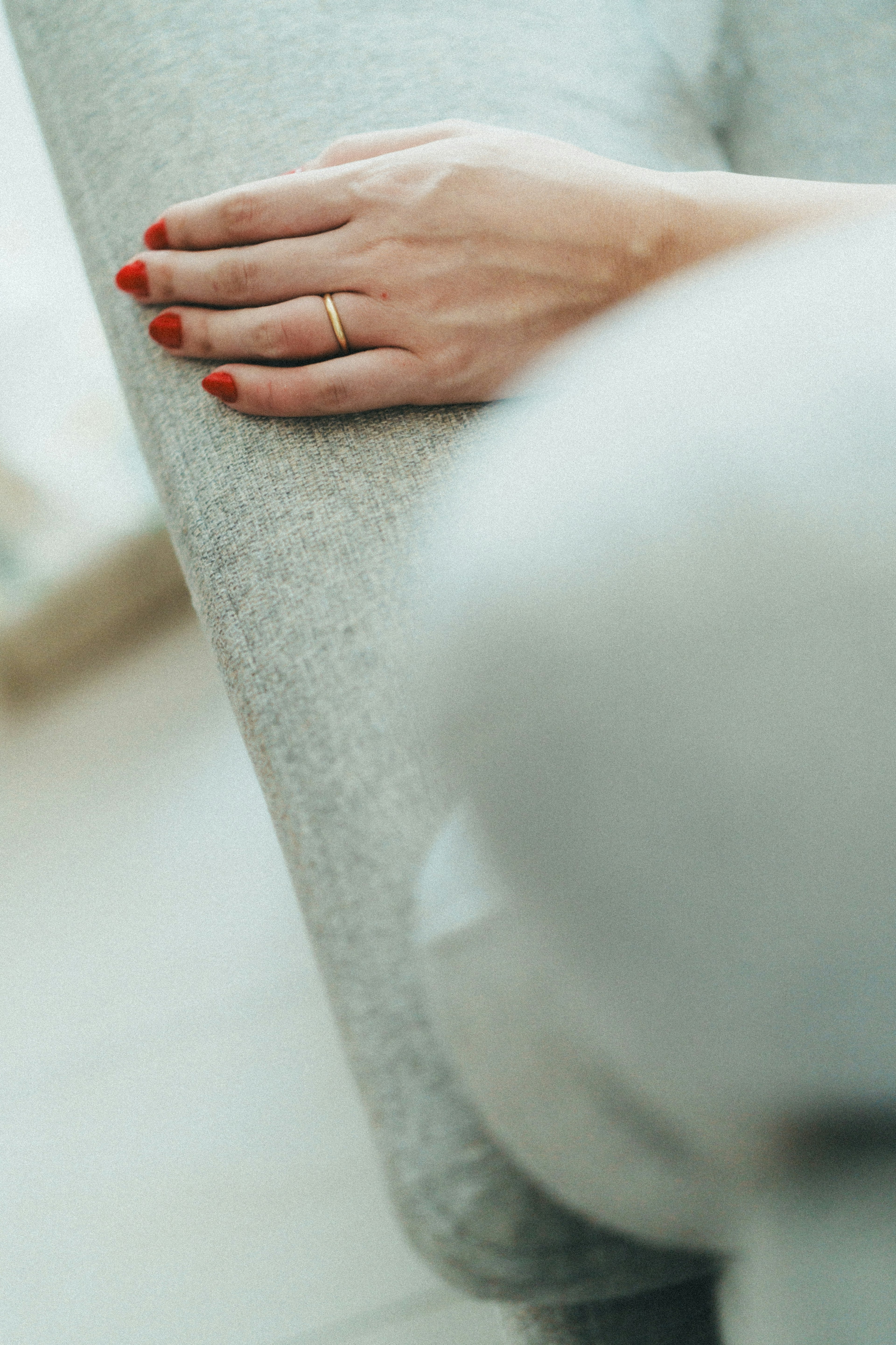 Primer plano de una mano descansando sobre un sofá gris con esmalte rojo