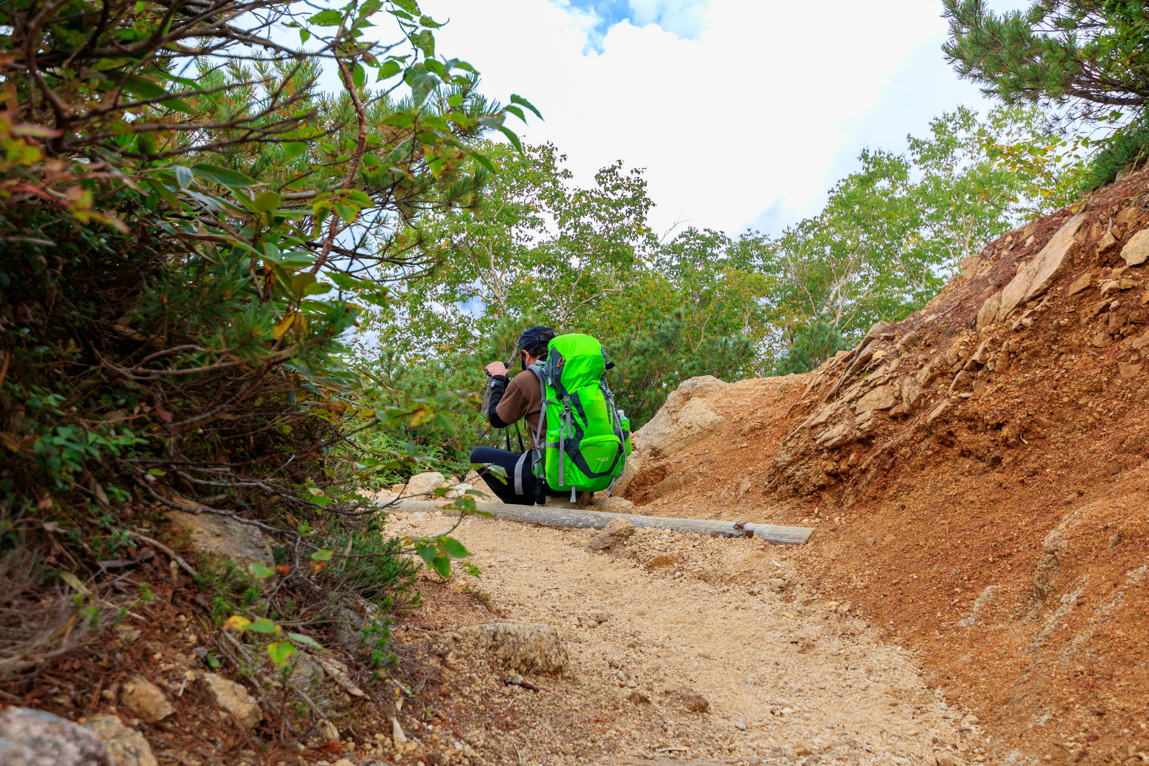 Un randonneur avec un sac à dos vert assis sur un sentier entouré d'arbres