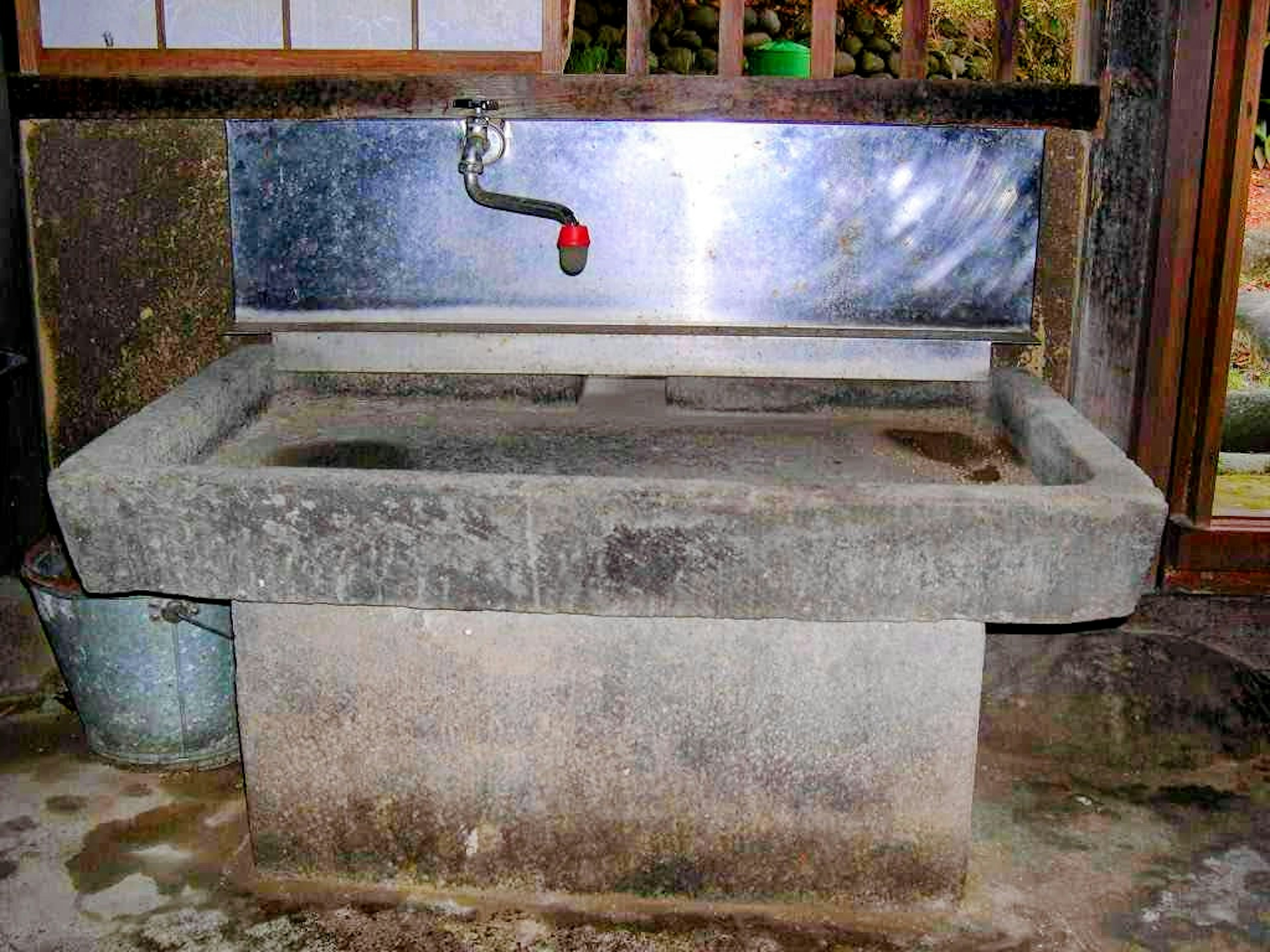 Antiguo lavabo de piedra con grifo de metal y fondo de madera