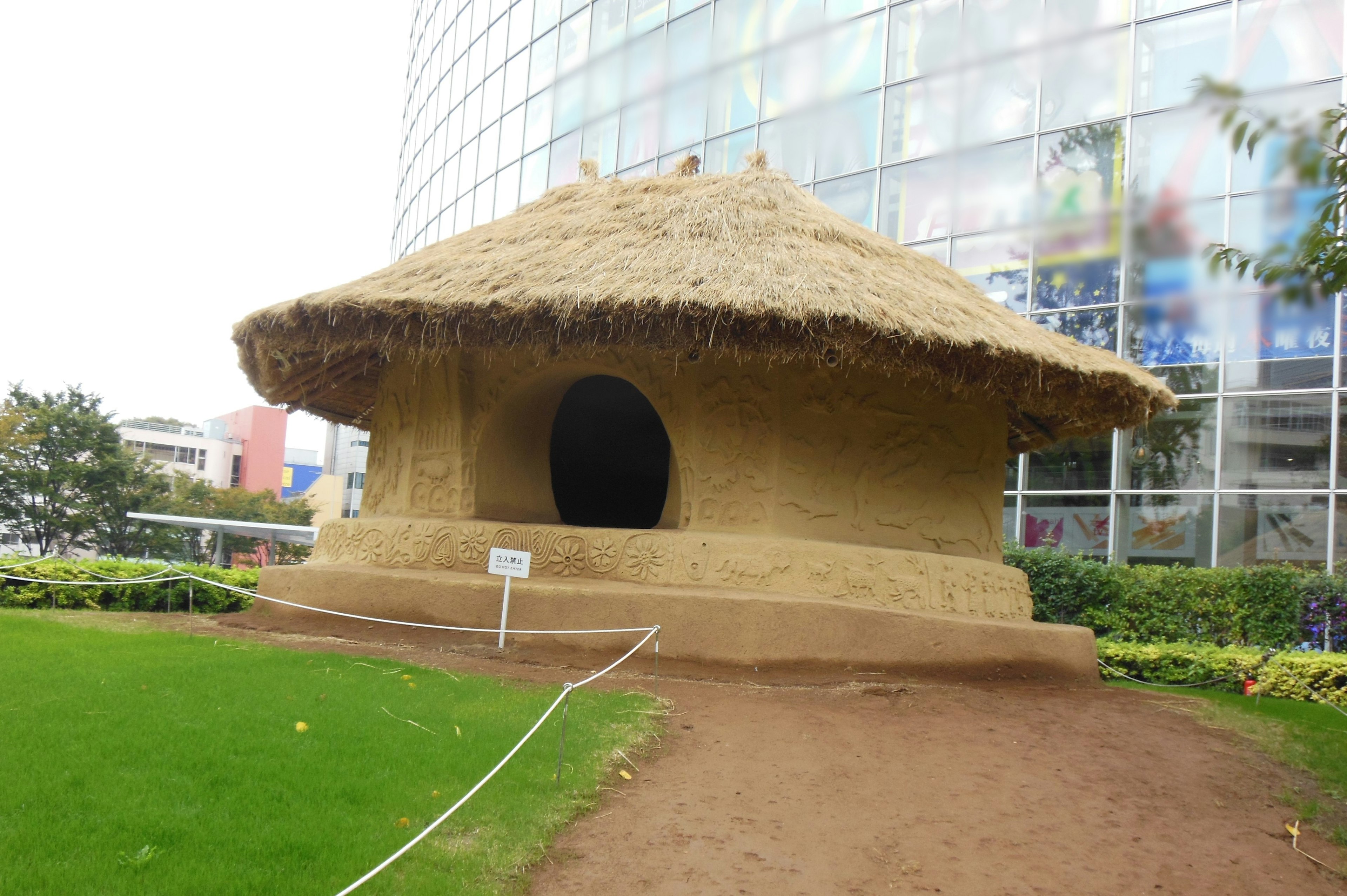 Traditional straw house contrasting with a modern glass building