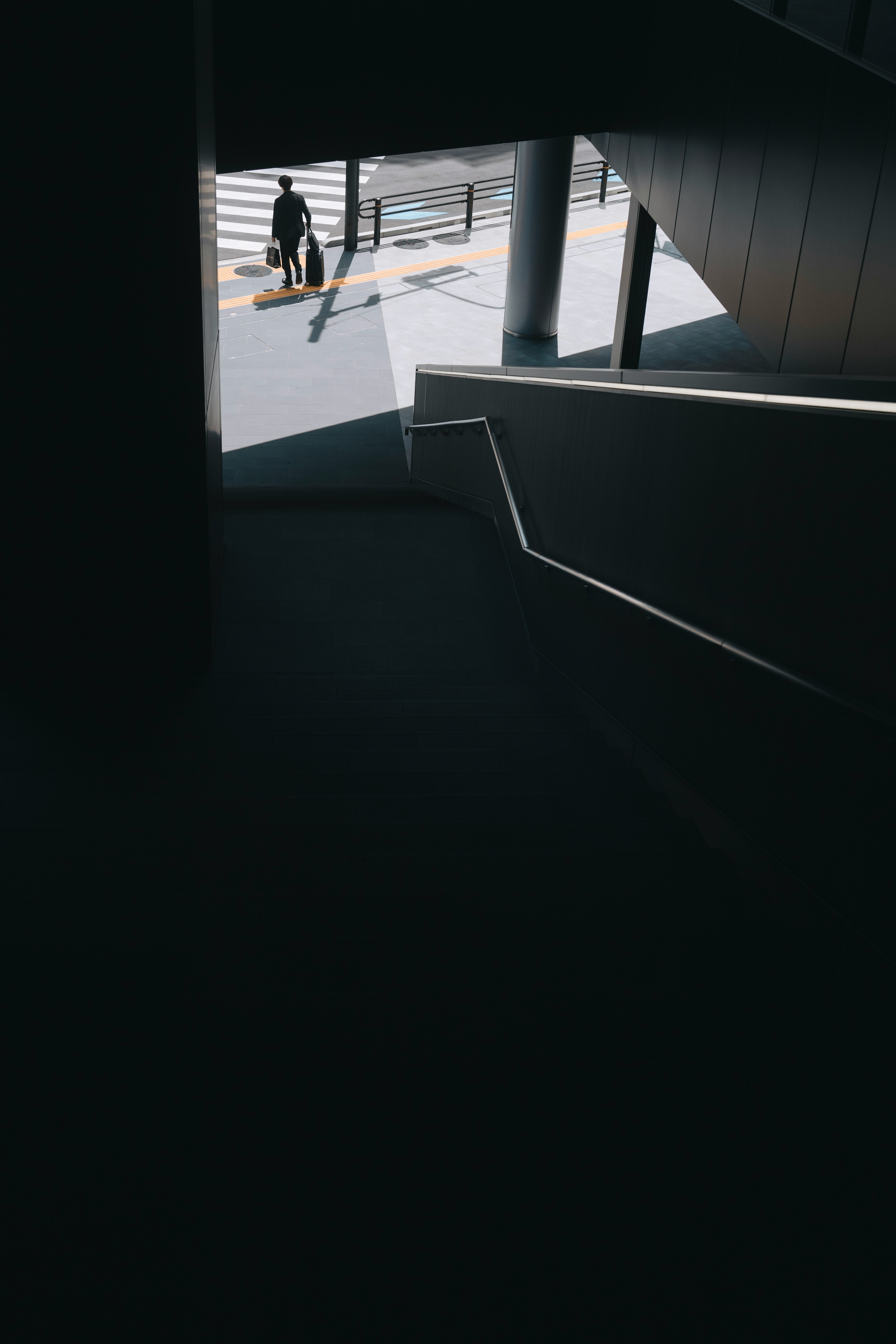 A silhouette of a person walking outside seen from a dark staircase