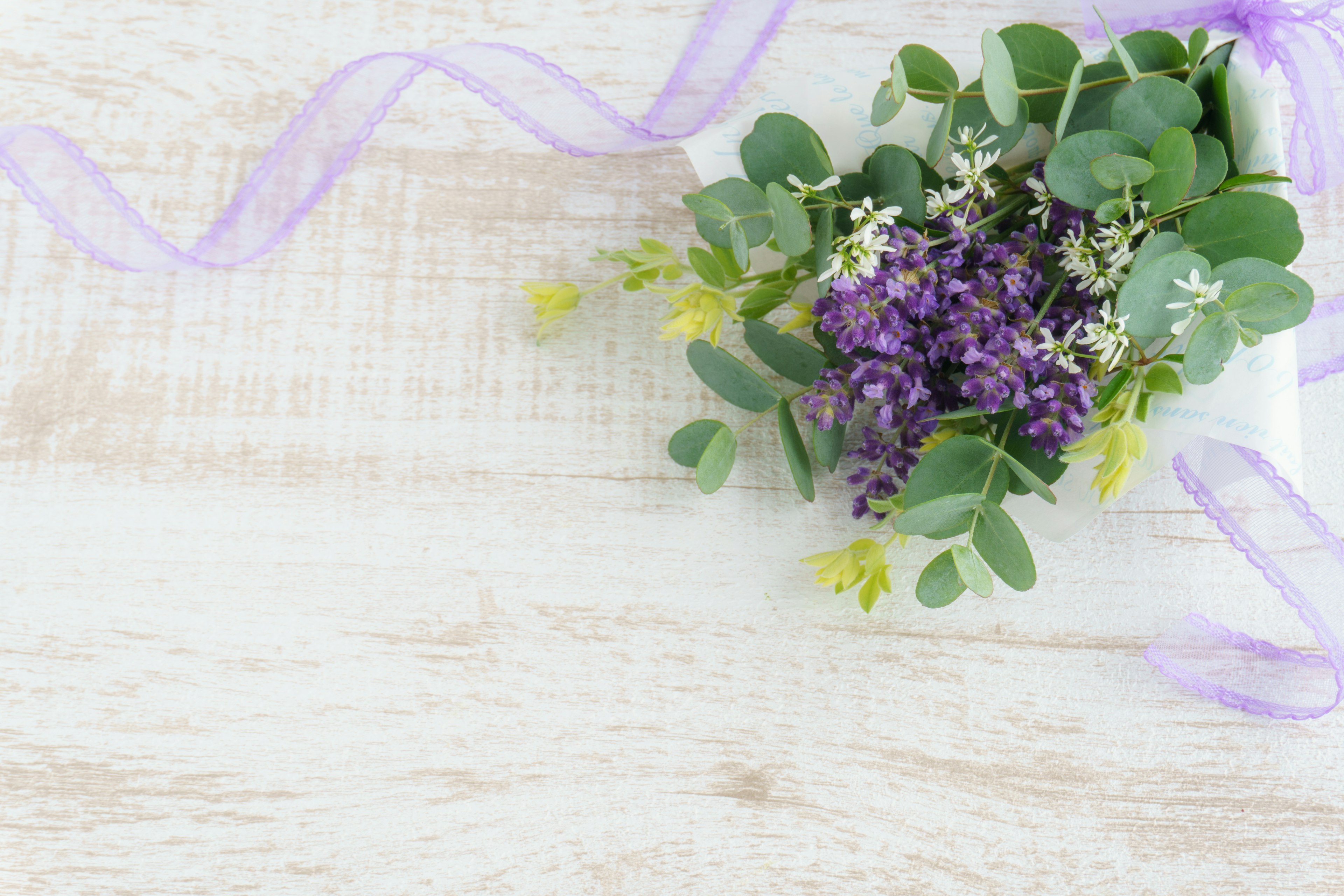 Ramo de flores moradas y hojas verdes con una cinta morada sobre una superficie de madera