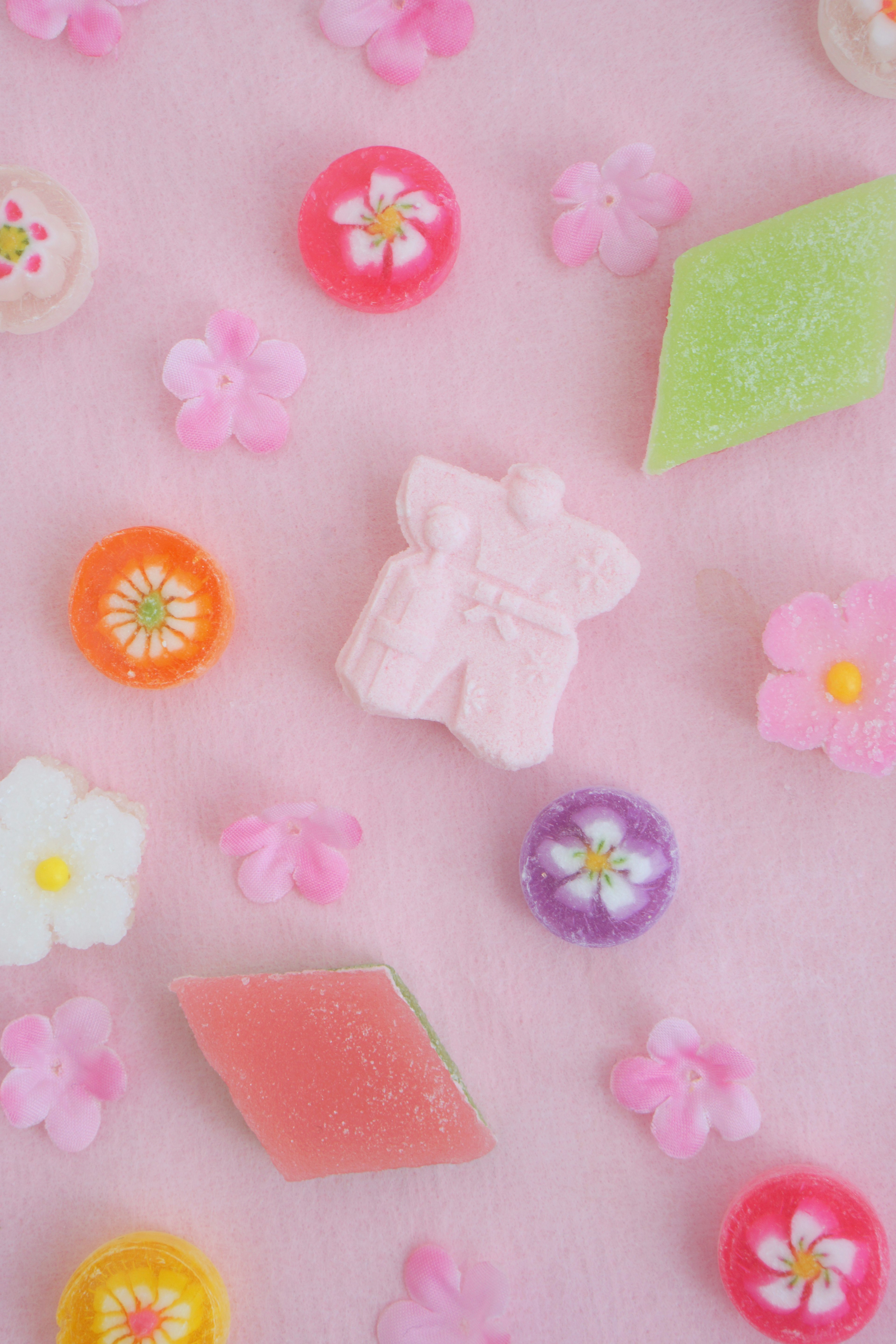 Dulces japoneses coloridos y motivos florales esparcidos sobre un fondo rosa