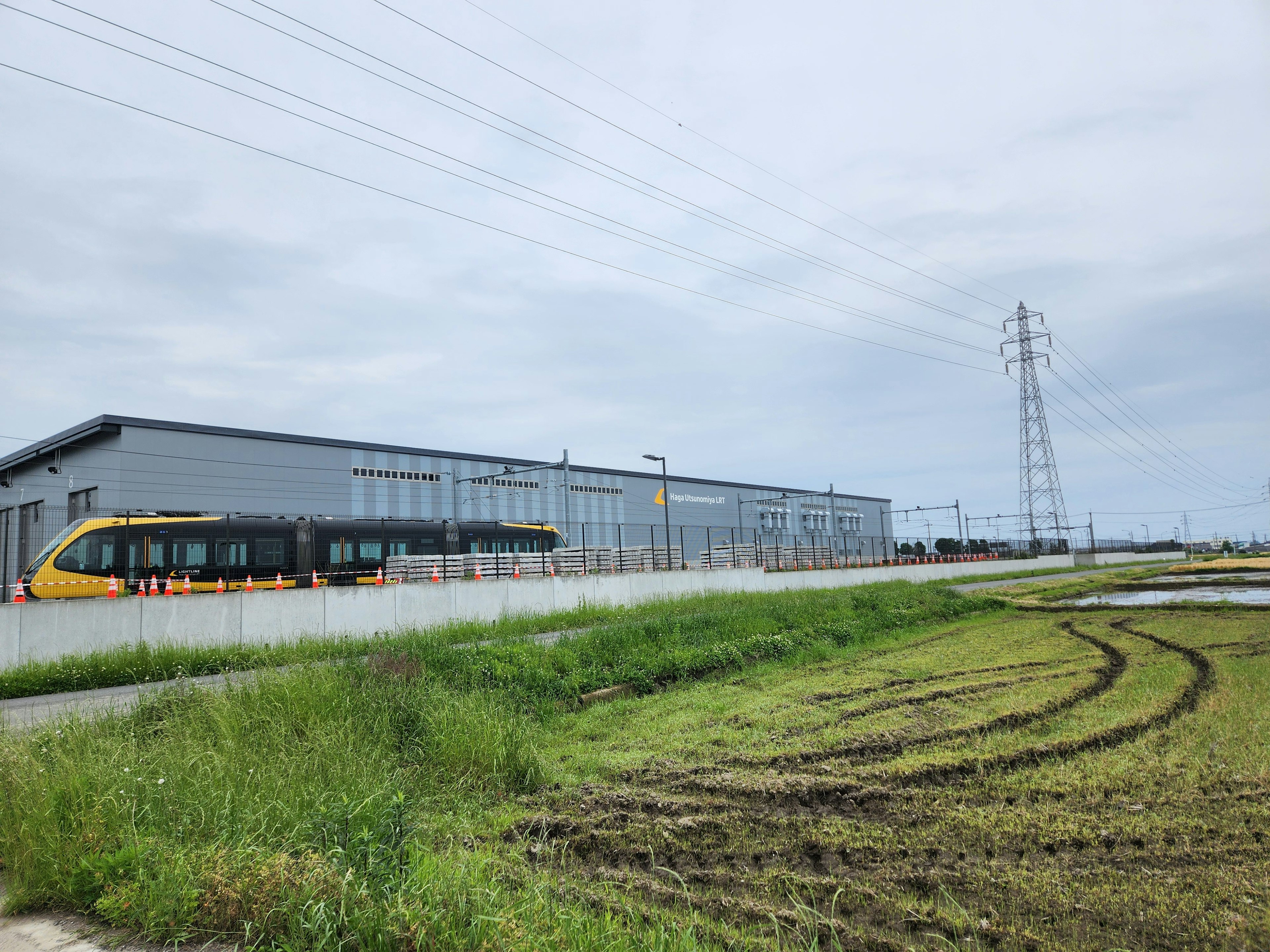 Vue d'une usine avec un train à proximité herbe verte et lignes électriques visibles