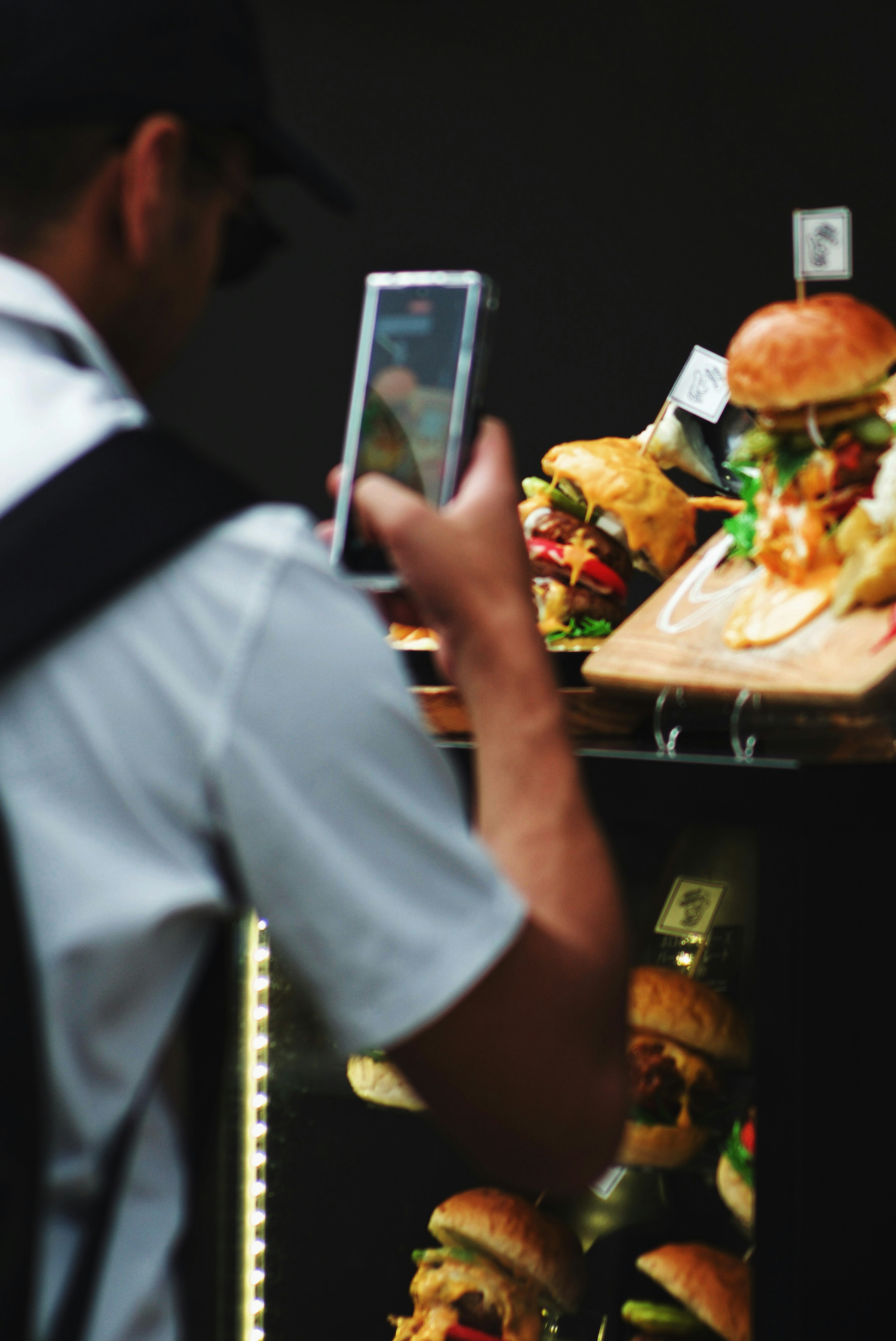 Man taking a photo of delicious burgers displayed in a showcase