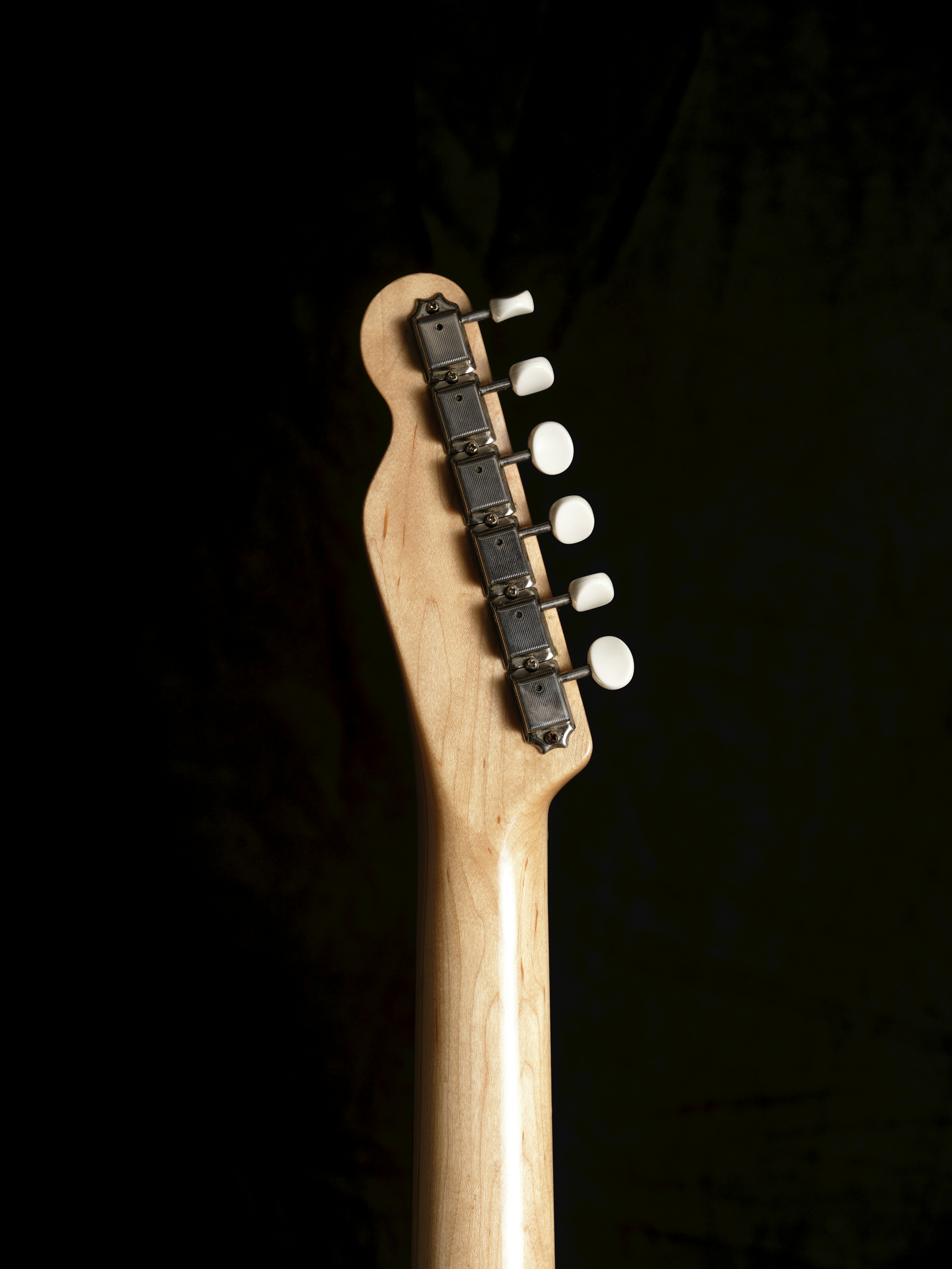 Side view of a guitar headstock against a black background