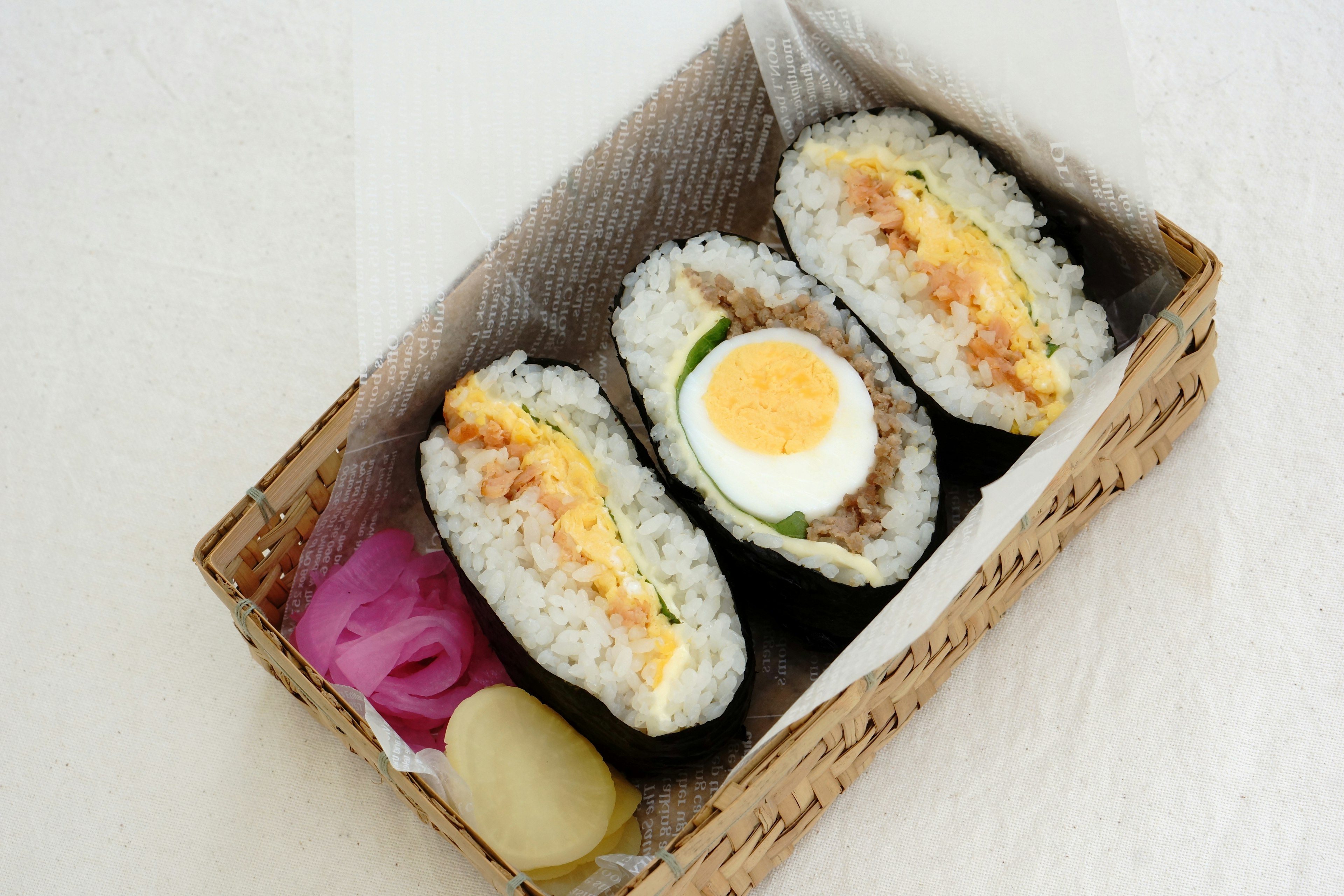 A photo of three types of sushi in a bento box featuring a sushi topped with an egg in the center meat sushi on the right and vegetable sushi with egg on the left accompanied by pink ginger and yellow radish