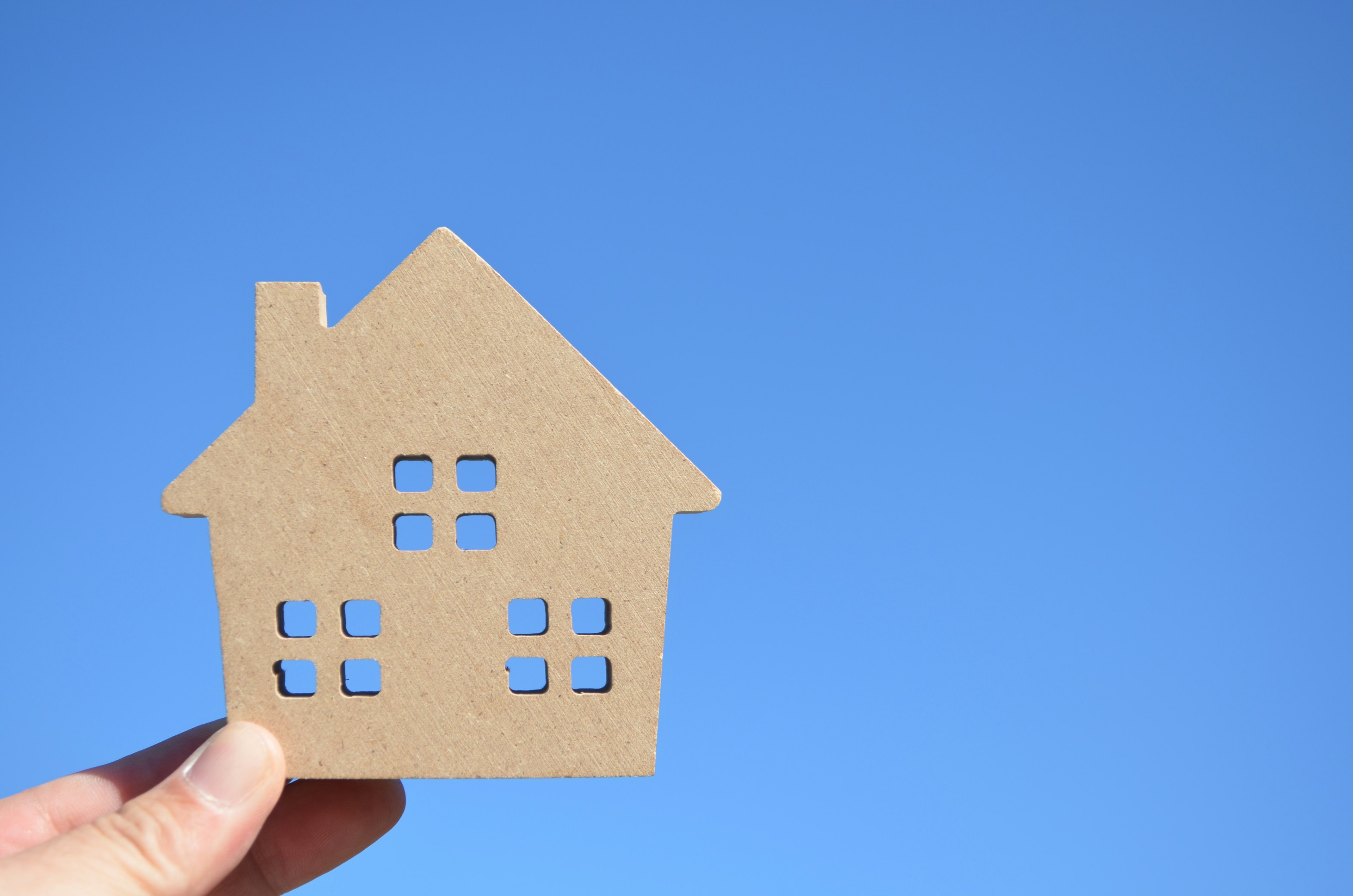 Una mano che tiene un modello di casa in carta marrone contro un cielo blu