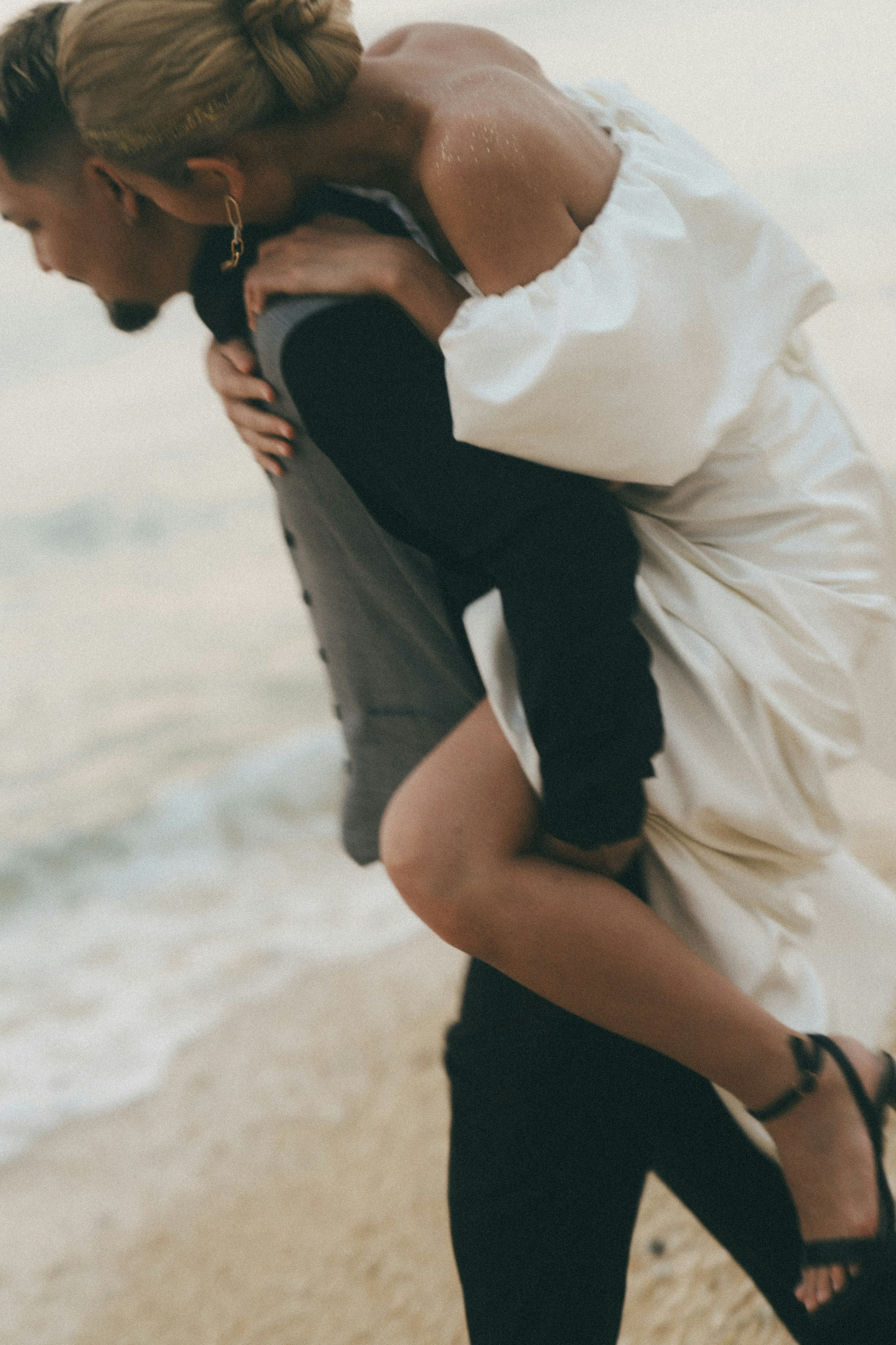 Un hombre cargando a una mujer con vestido blanco en la playa