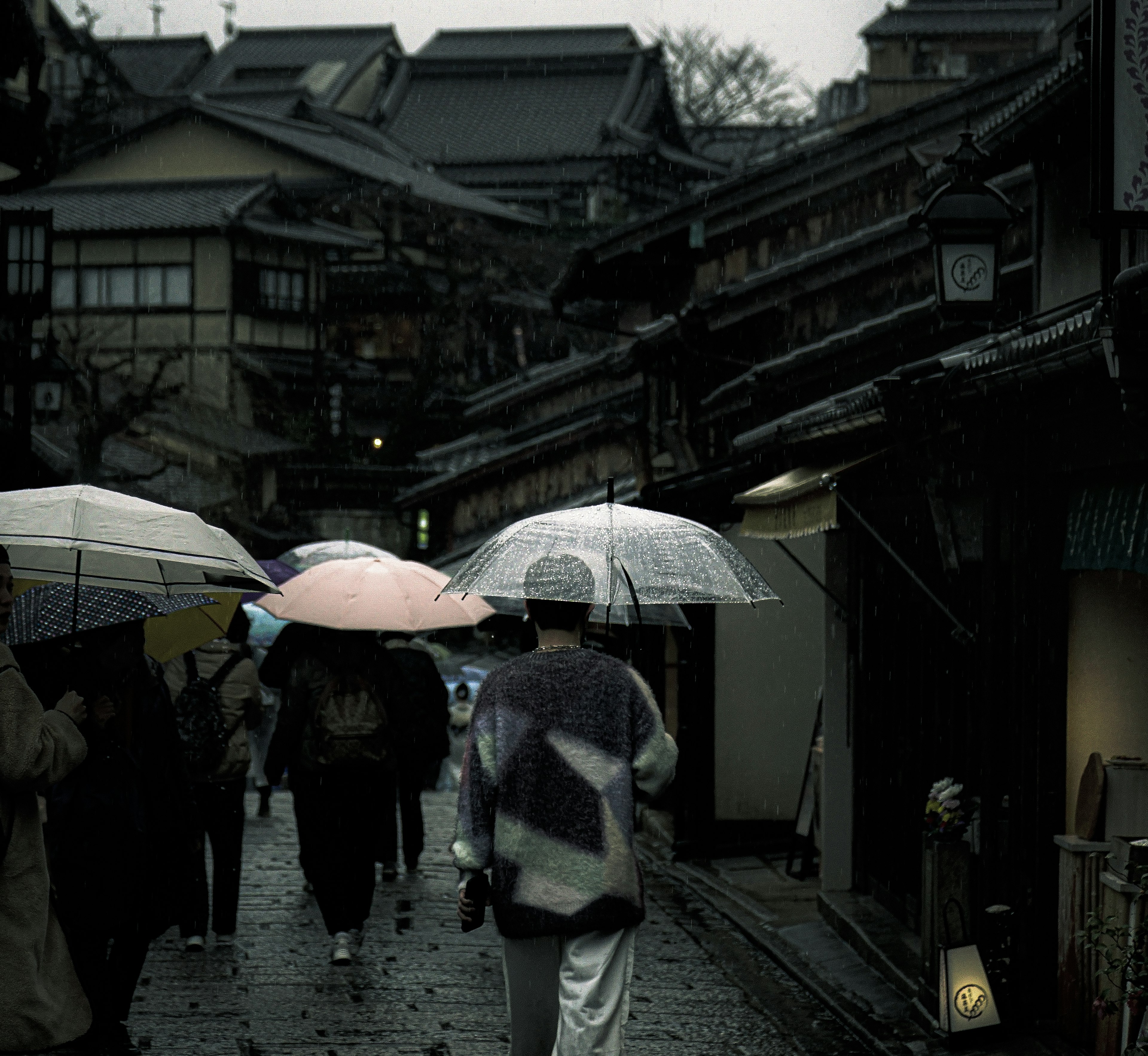 People walking with umbrellas in a traditional street under rain