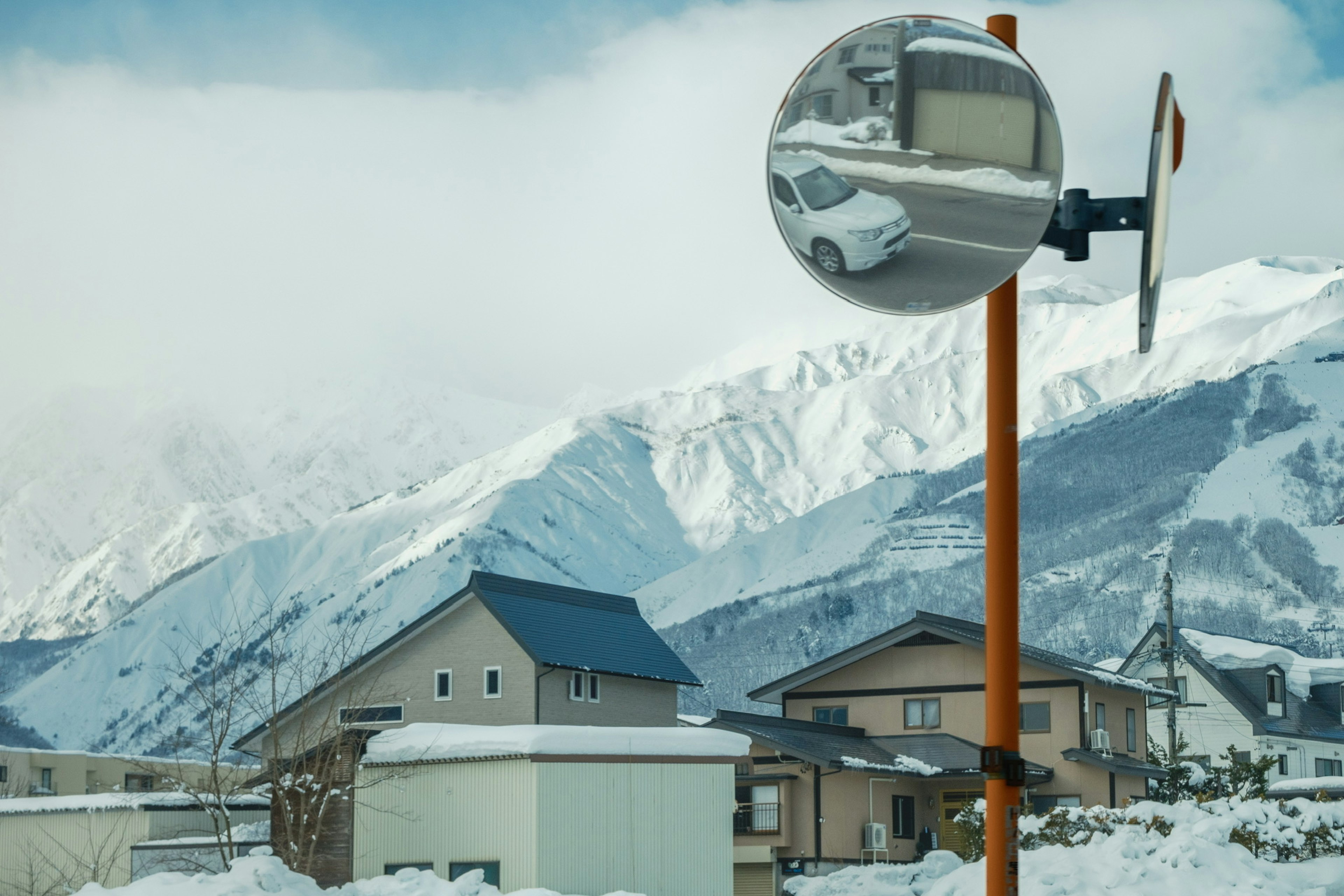 雪に覆われた山々と住宅が映るミラー