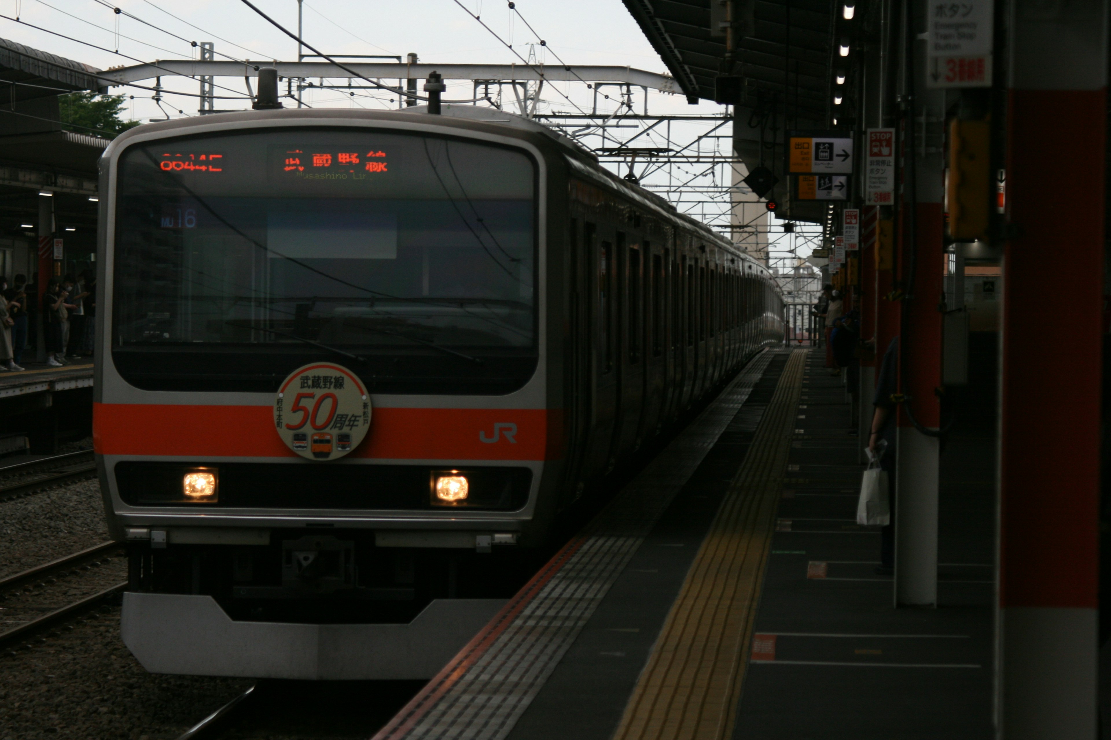 รถไฟญี่ปุ่นจอดที่สถานี มีโลโก้ด้านหน้าและไฟแดงติดอยู่