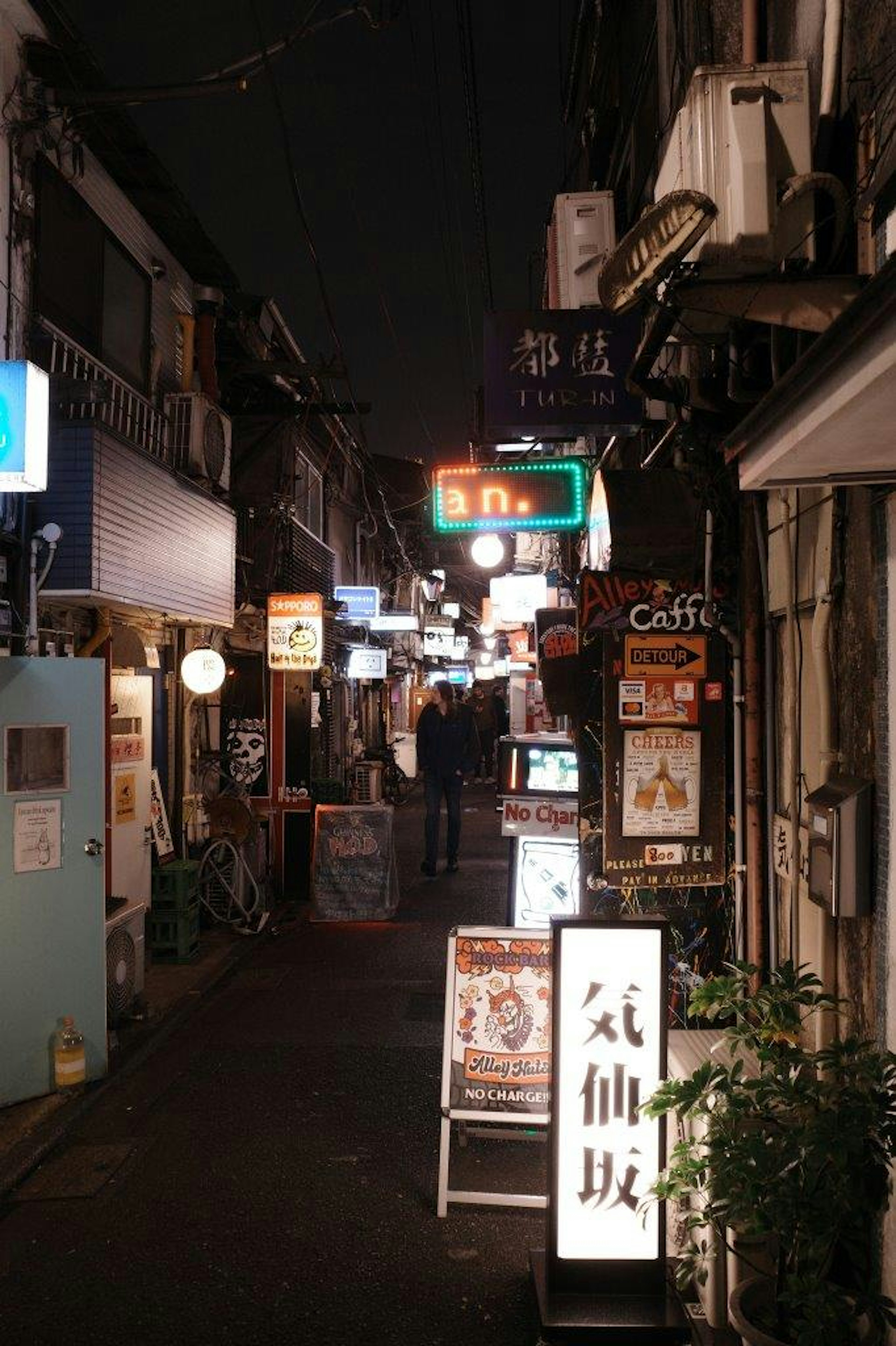 Callejón estrecho de noche con letreros de restaurantes y luces