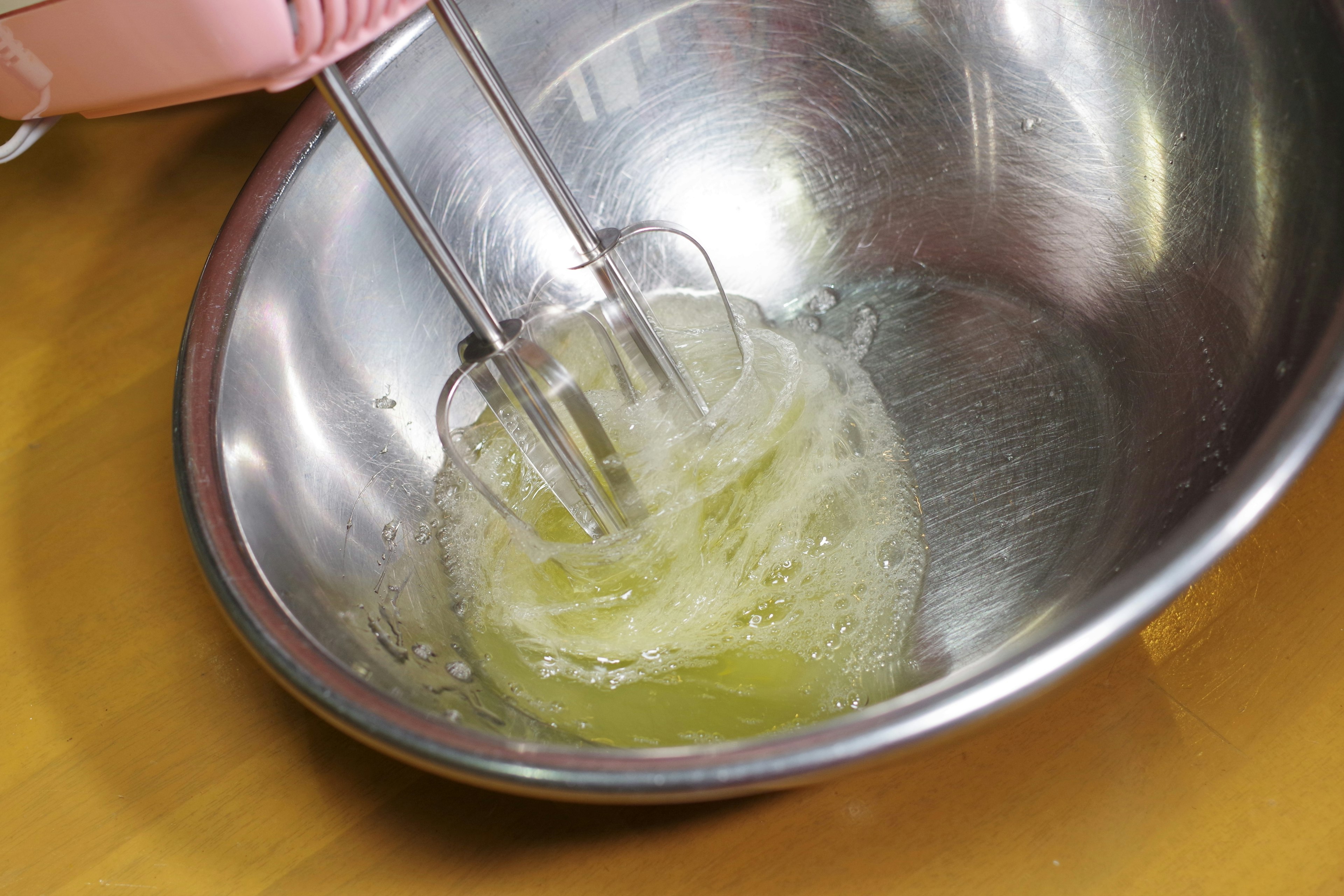 Hand mixer whipping egg whites in a metal bowl