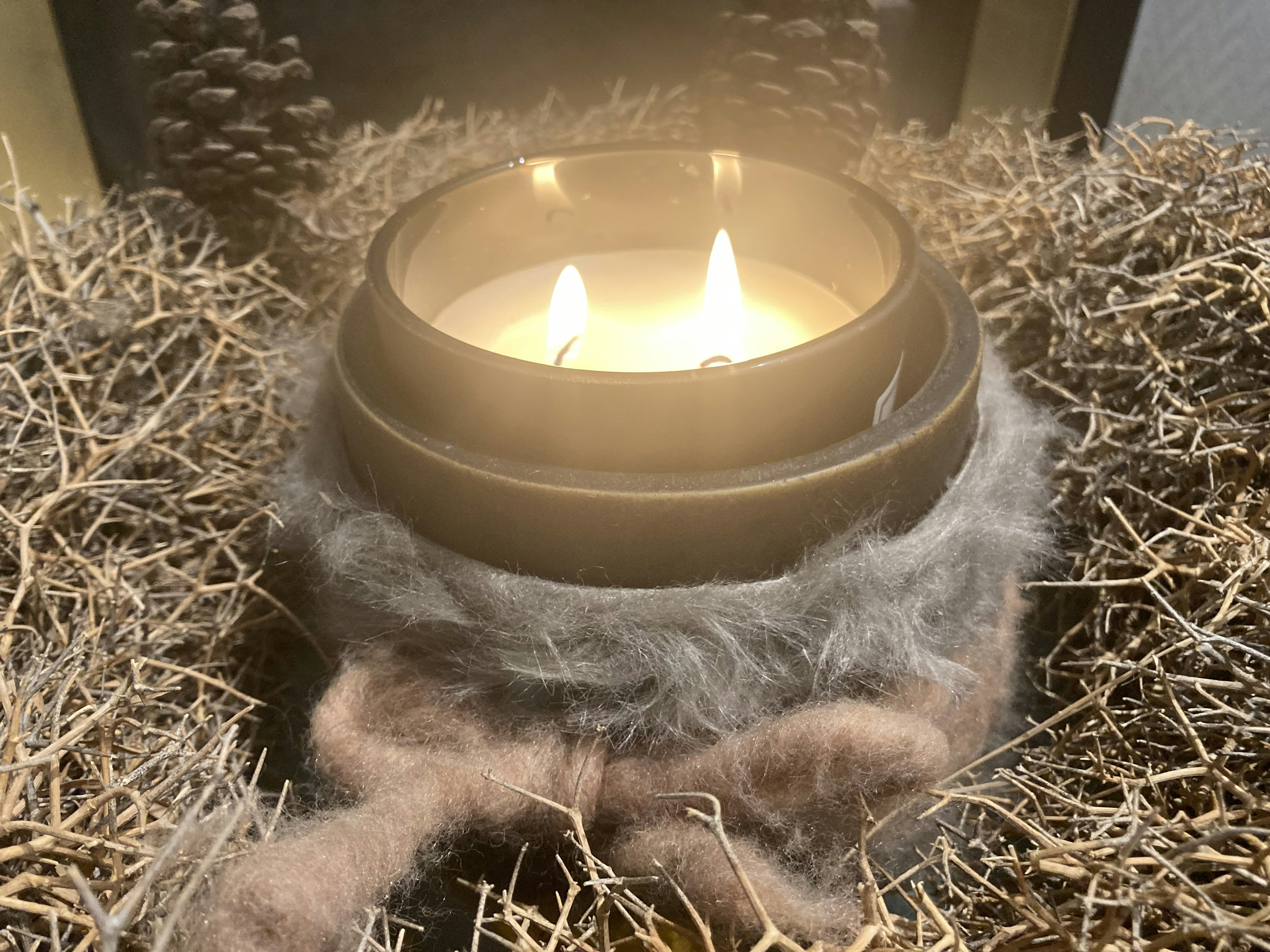 A cozy candle placed on hay with a soft wrap