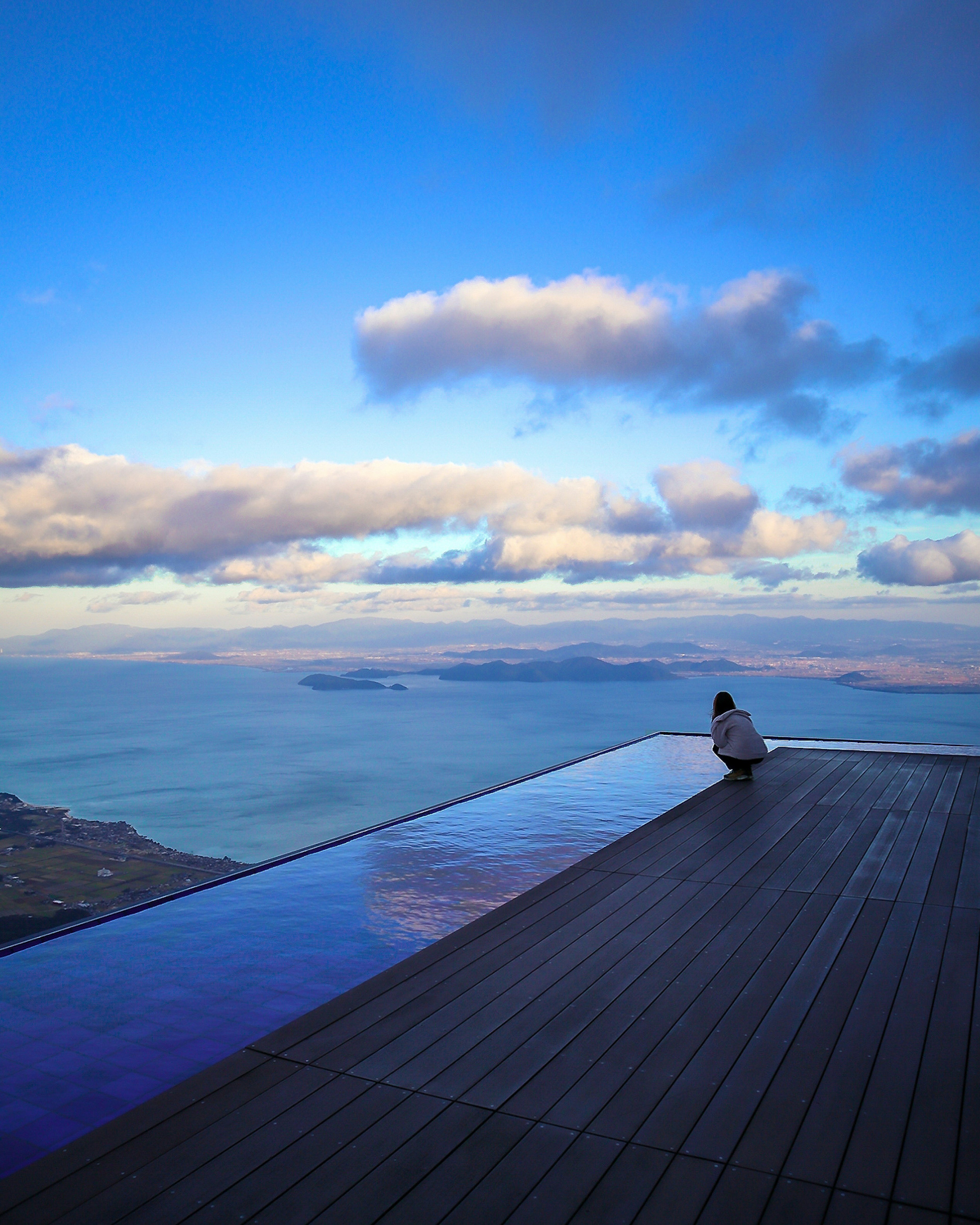 美しい海と空の景色を背景に屋外プールの縁に座る人