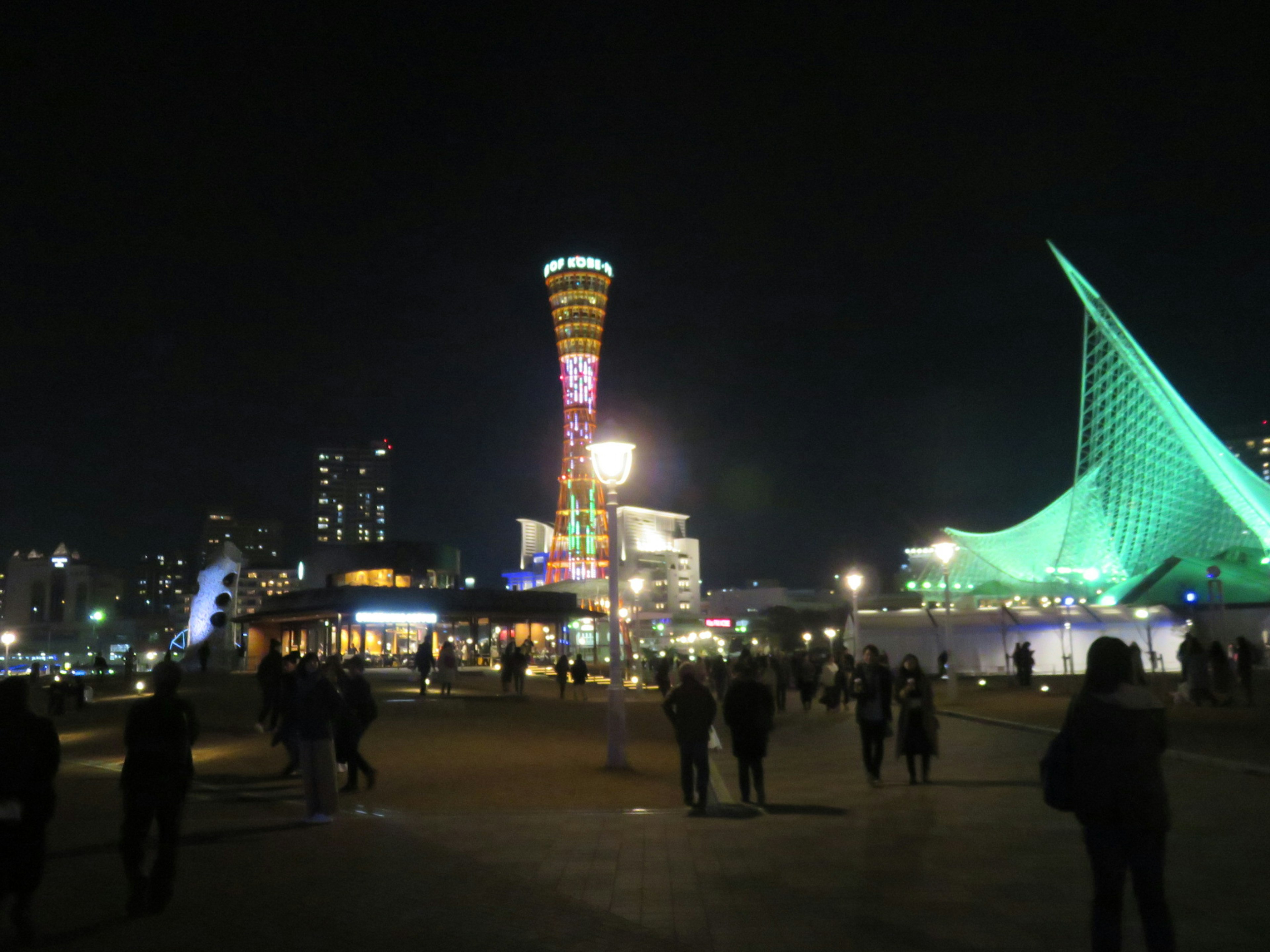 Paisaje nocturno de Kobe con la Torre Port y edificios Mosaic arquitectura verde y siluetas de personas