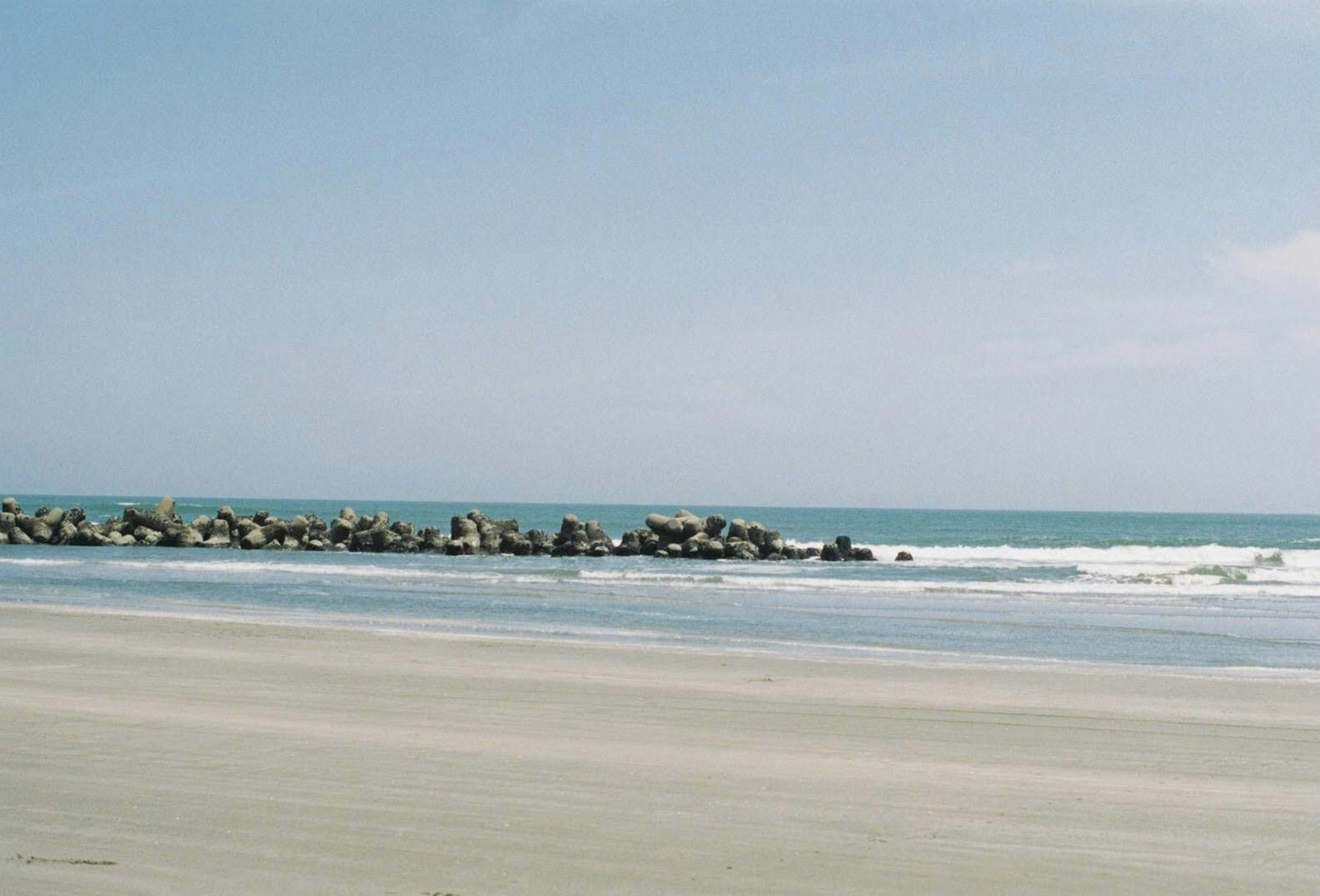 ทิวทัศน์ชายหาดทรายและทะเลสงบ มีเขื่อนหินมองเห็นได้