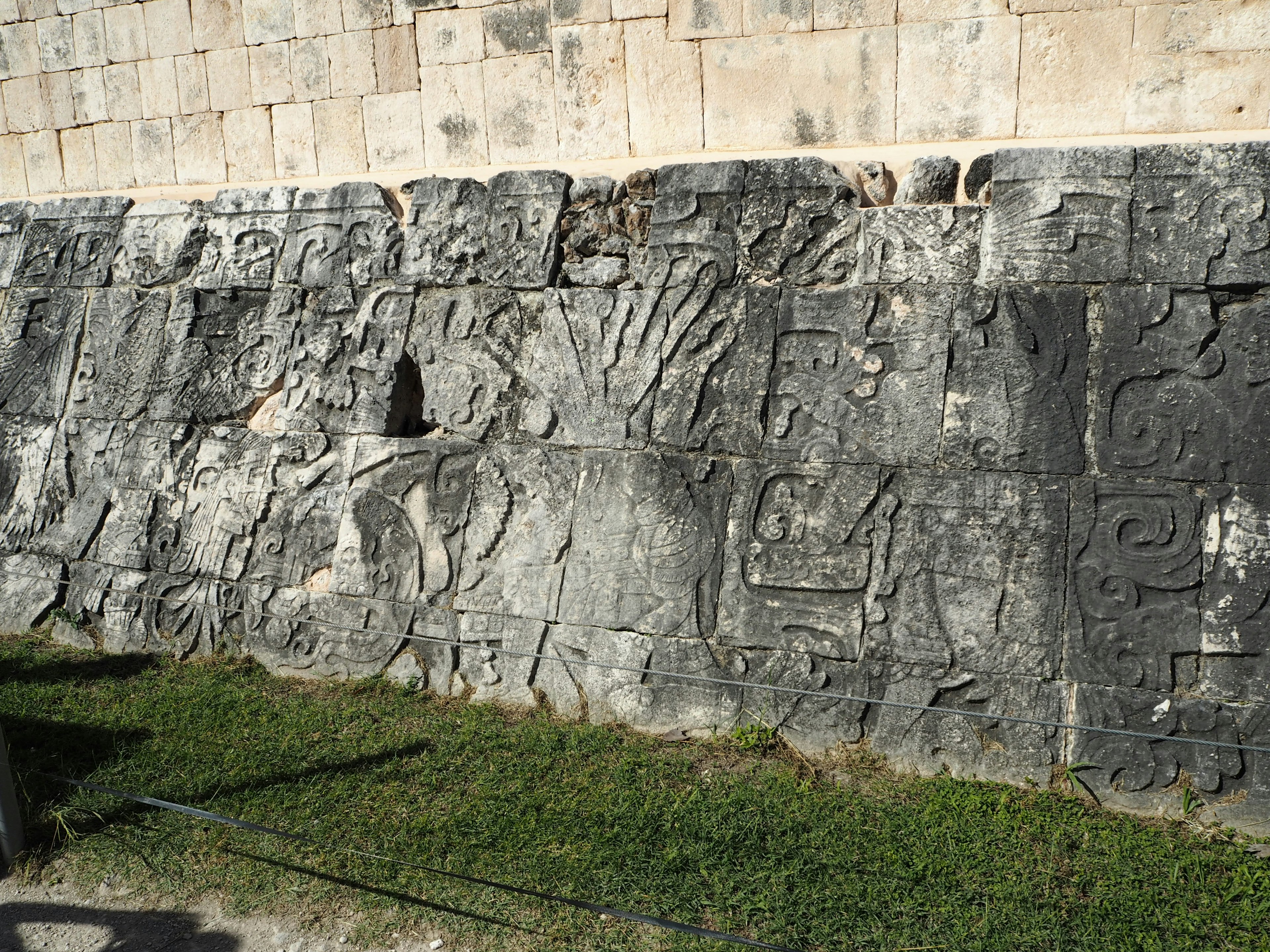 Ancient carved stone wall with intricate designs illuminated by sunlight and green grass