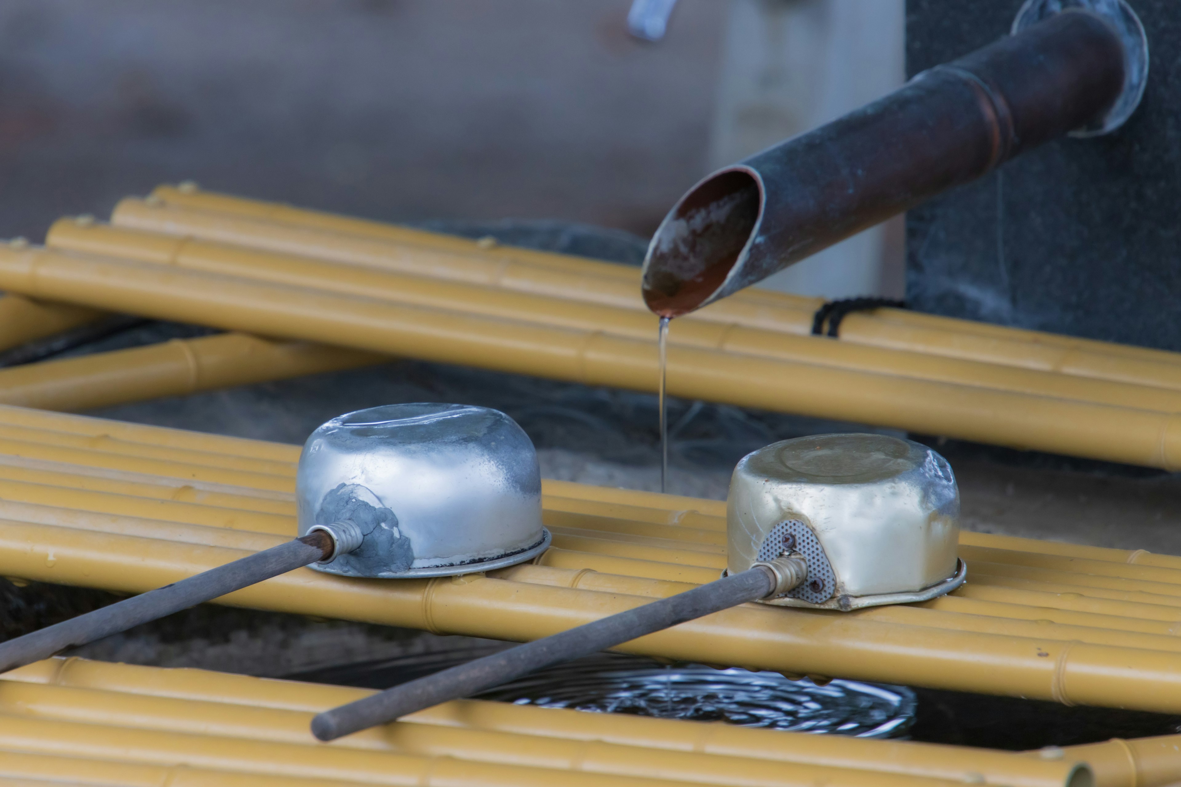 Szene mit Metallbehältern und Bambusstöcken mit fließendem Wasser