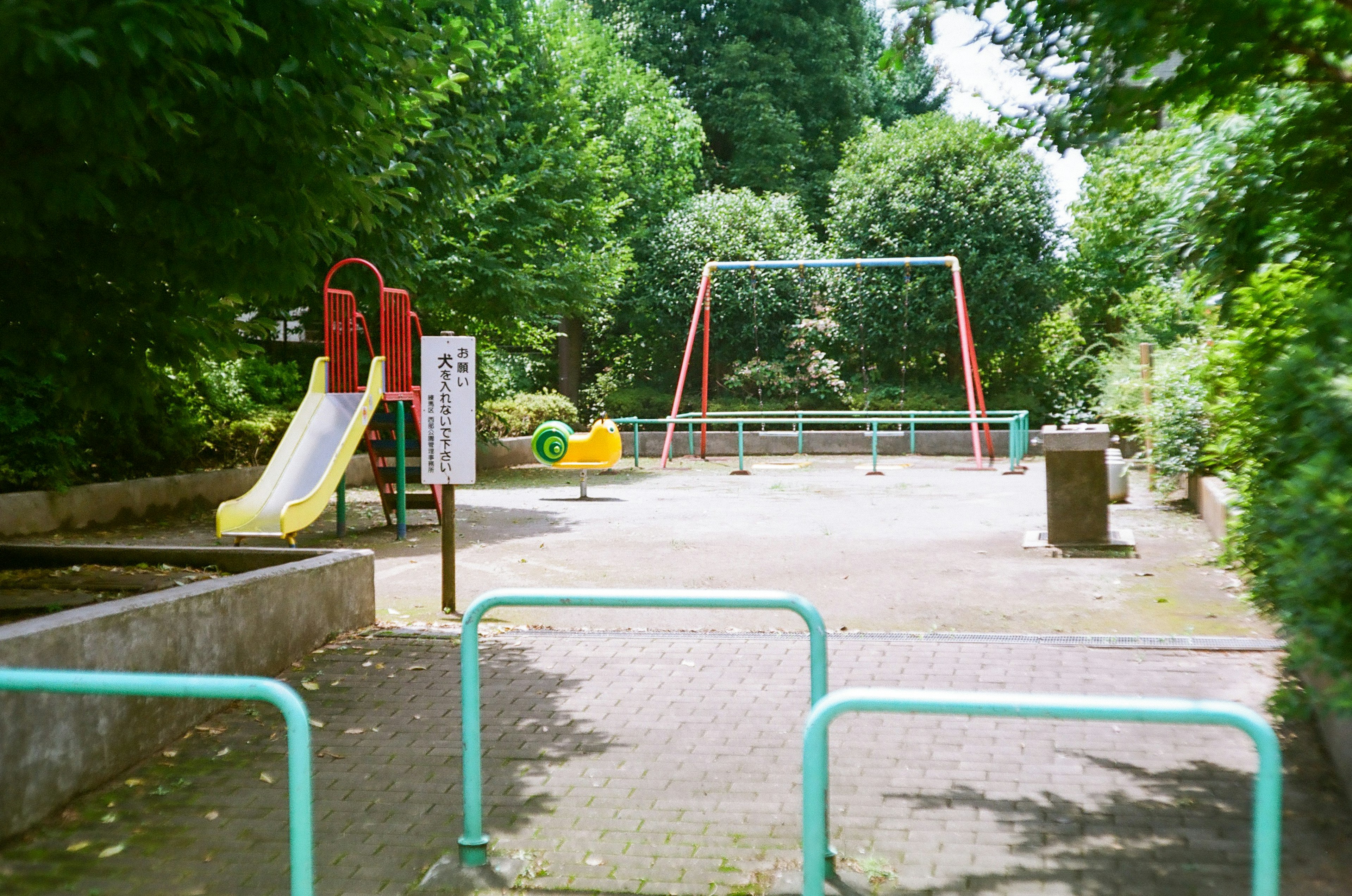 公園の遊び場にある黄色い滑り台と赤いブランコと緑の遊具