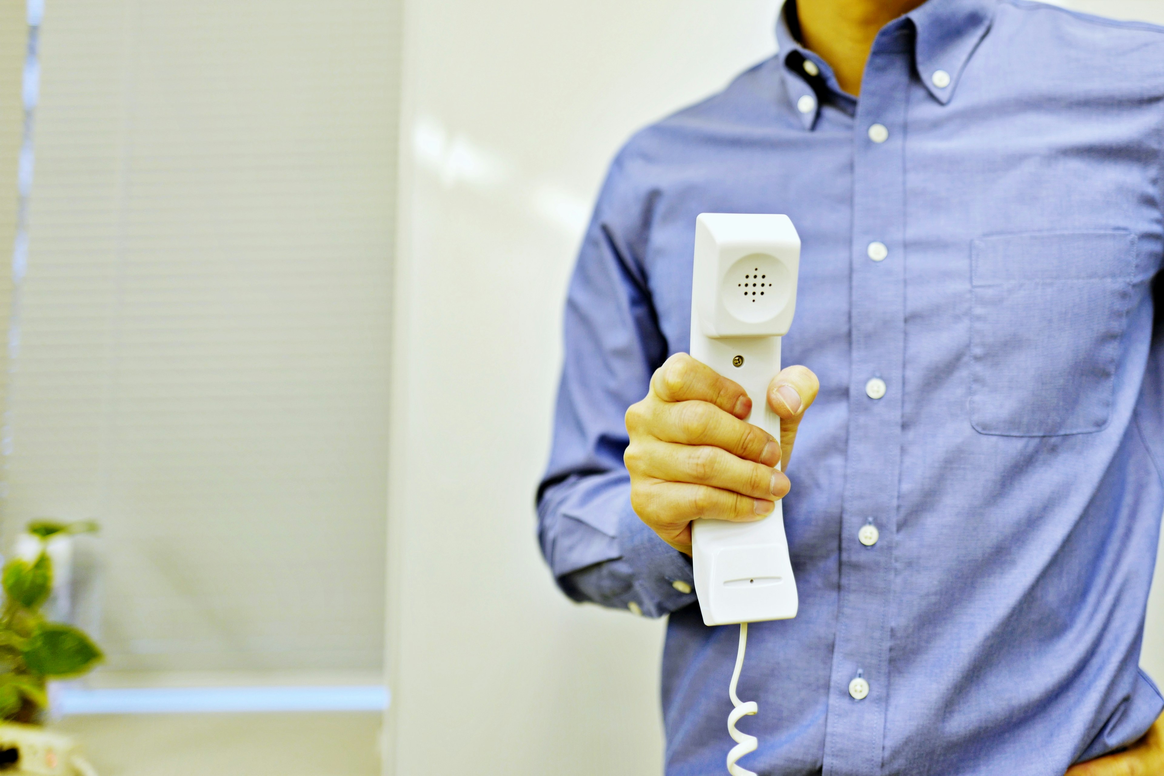 Man holding a telephone receiver in front of a white wall