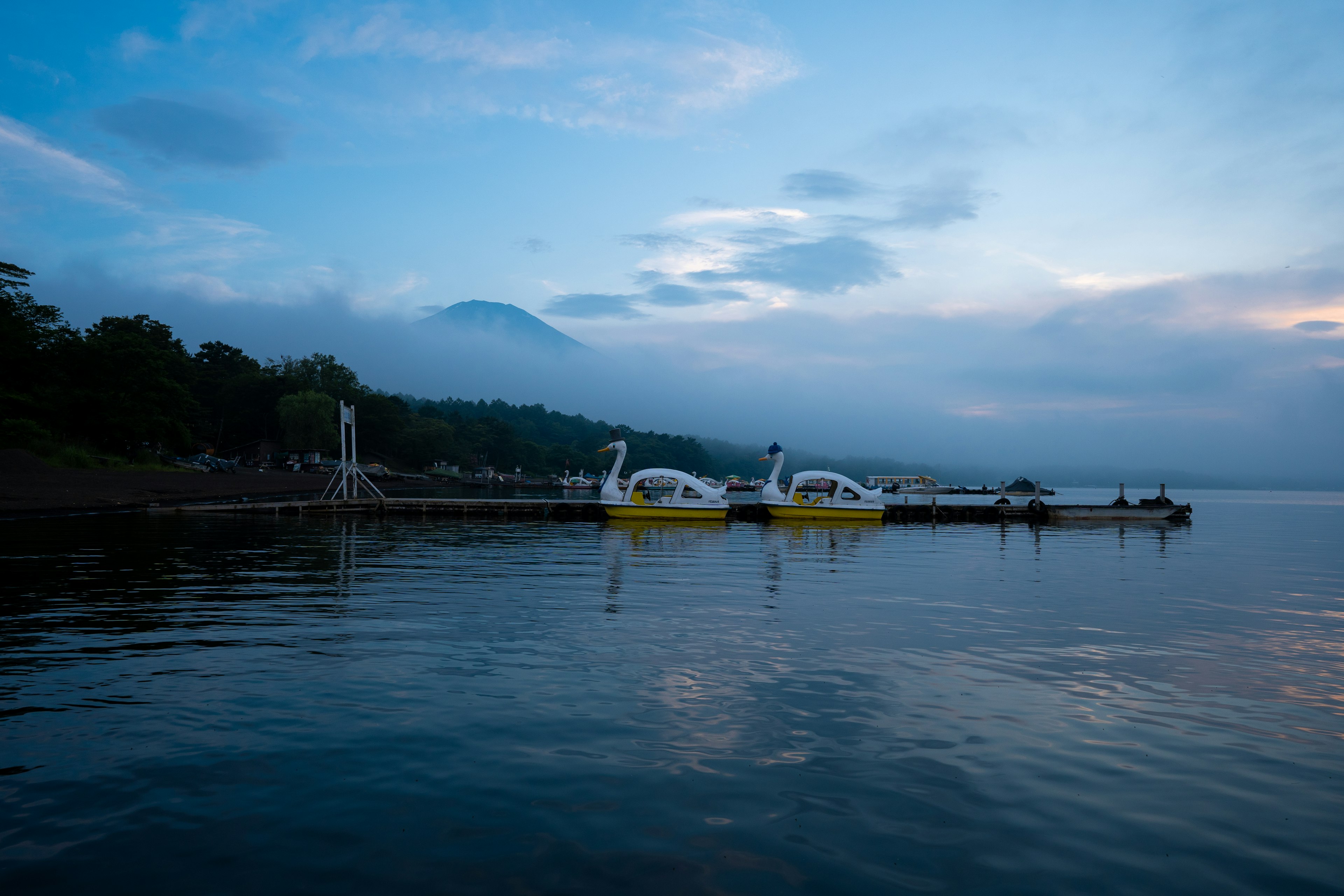 Danau tenang dengan perahu berbentuk angsa kuning dan pegunungan berkabut