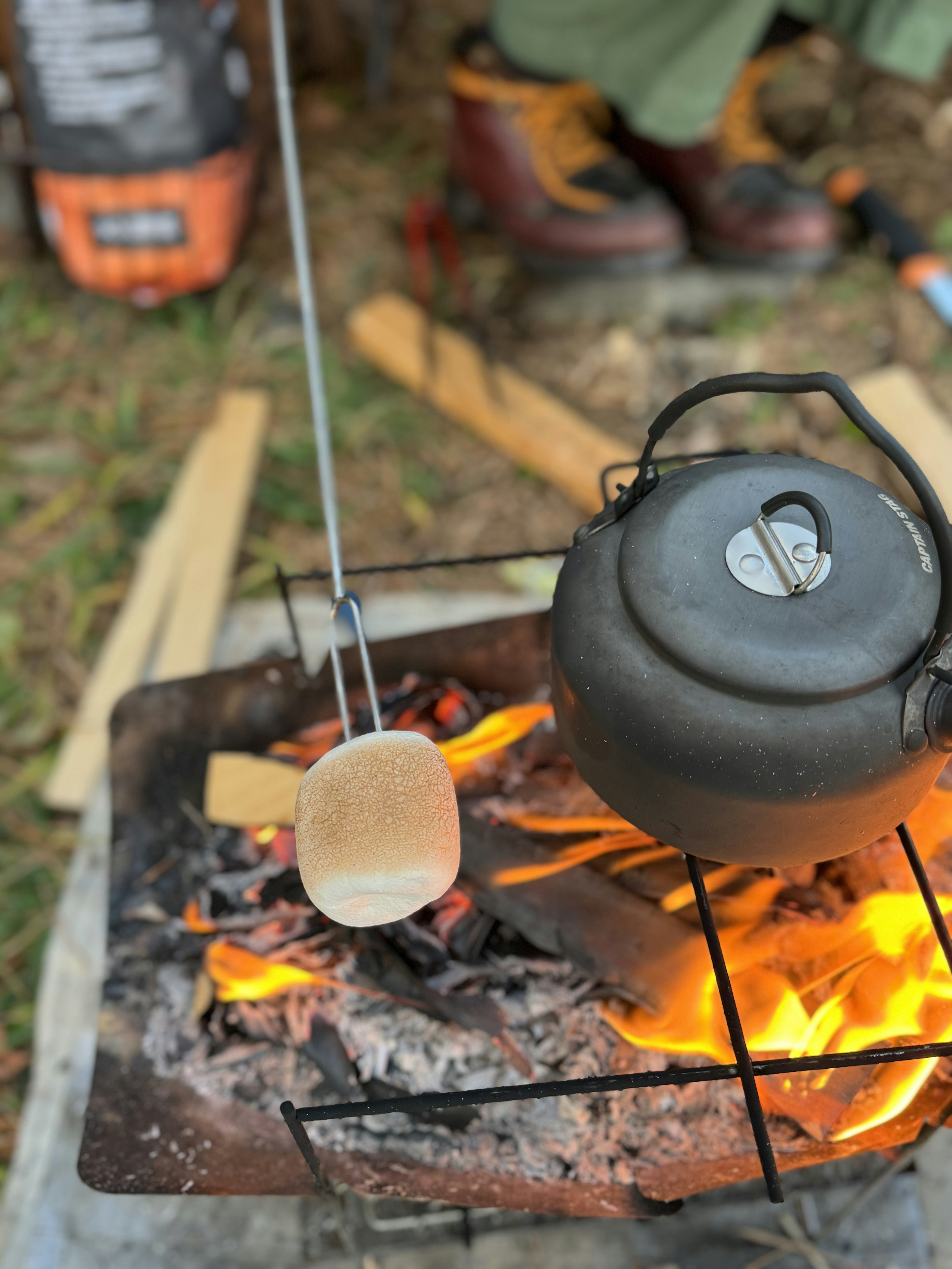 Ketel hitam di atas api unggun dengan tongkat untuk memanggang marshmallow