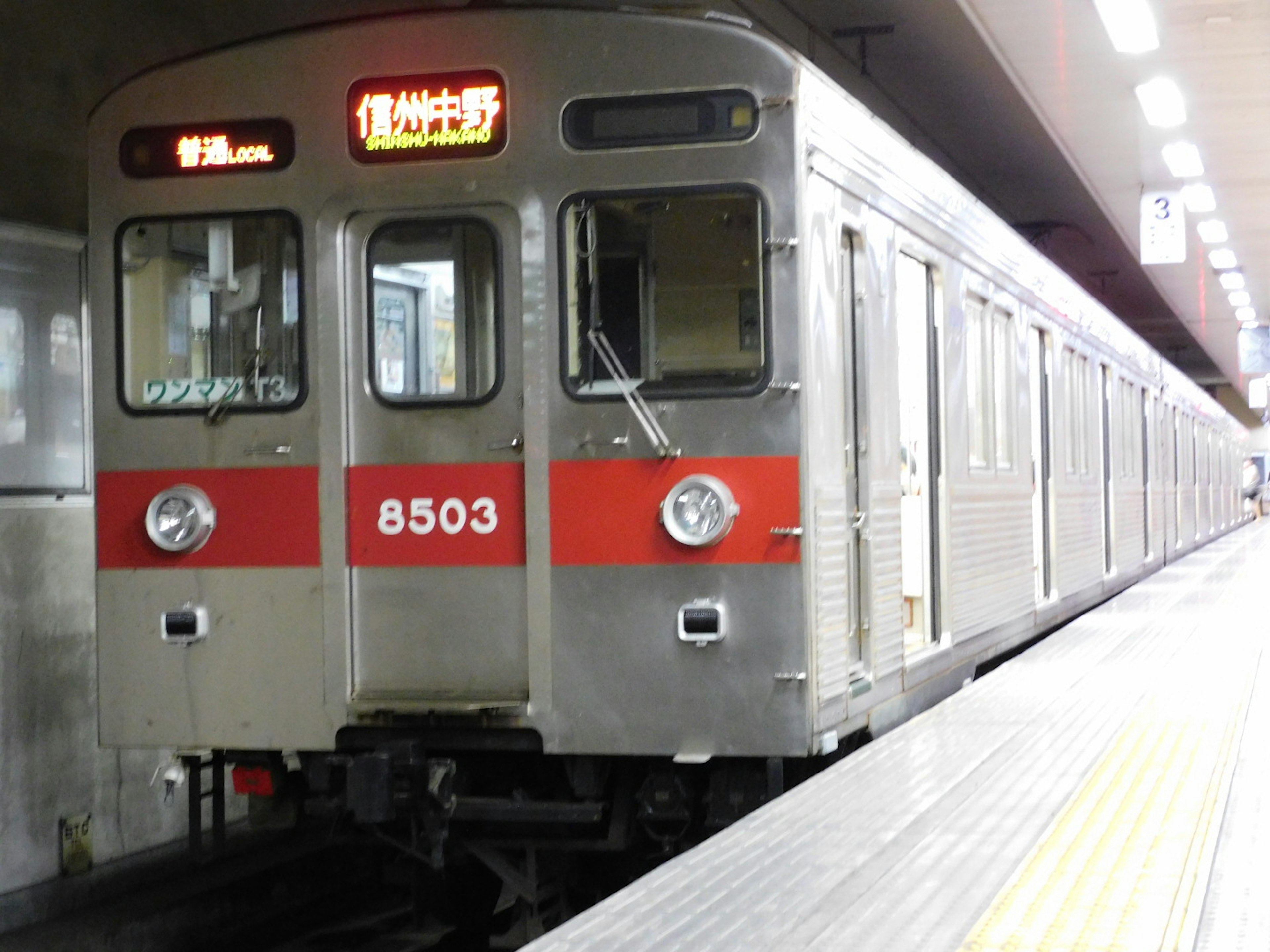 Tren de metro plateado con franjas rojas detenido en la estación