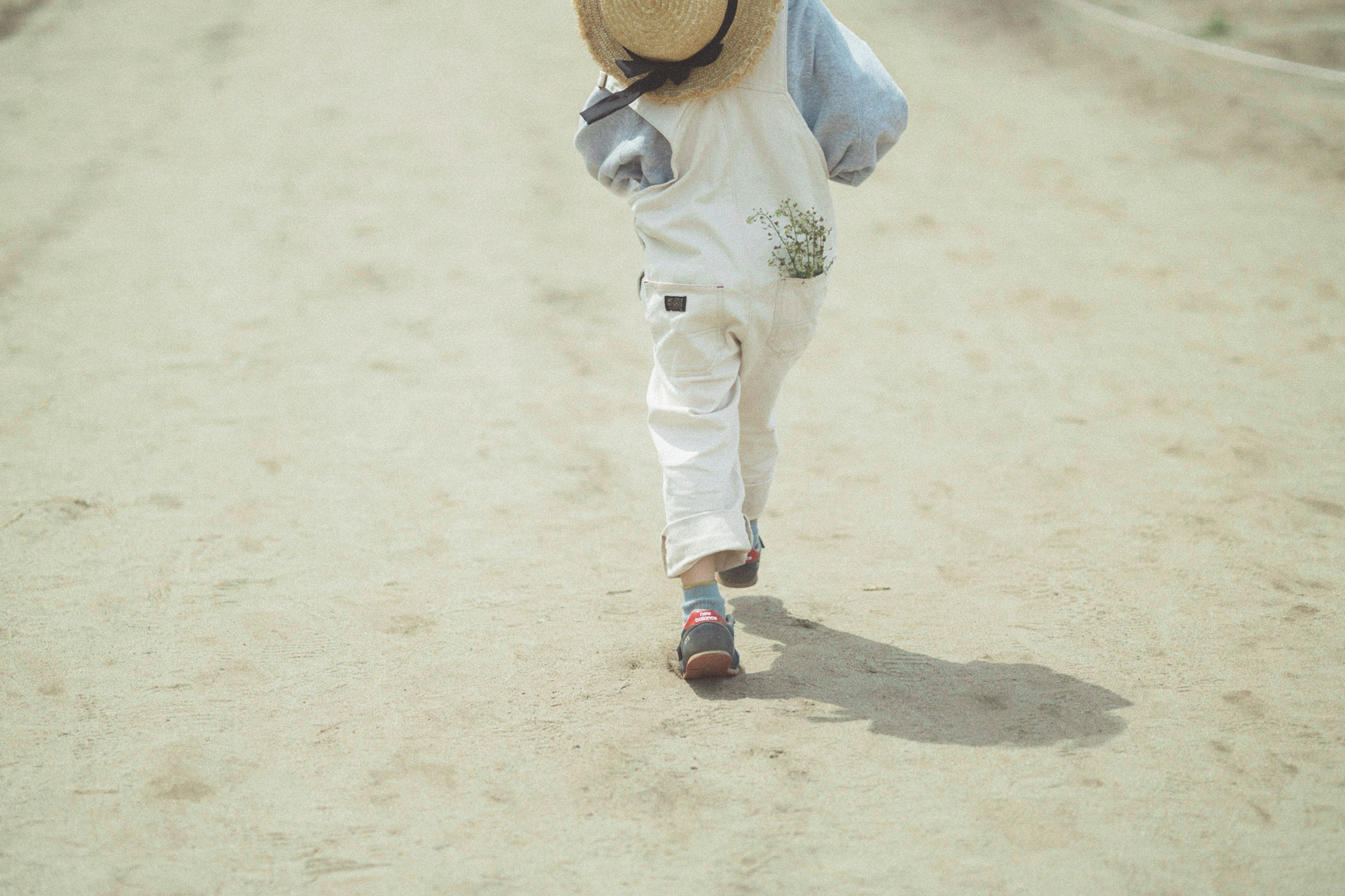 Bambino con un cappello di paglia che cammina su un sentiero di sabbia