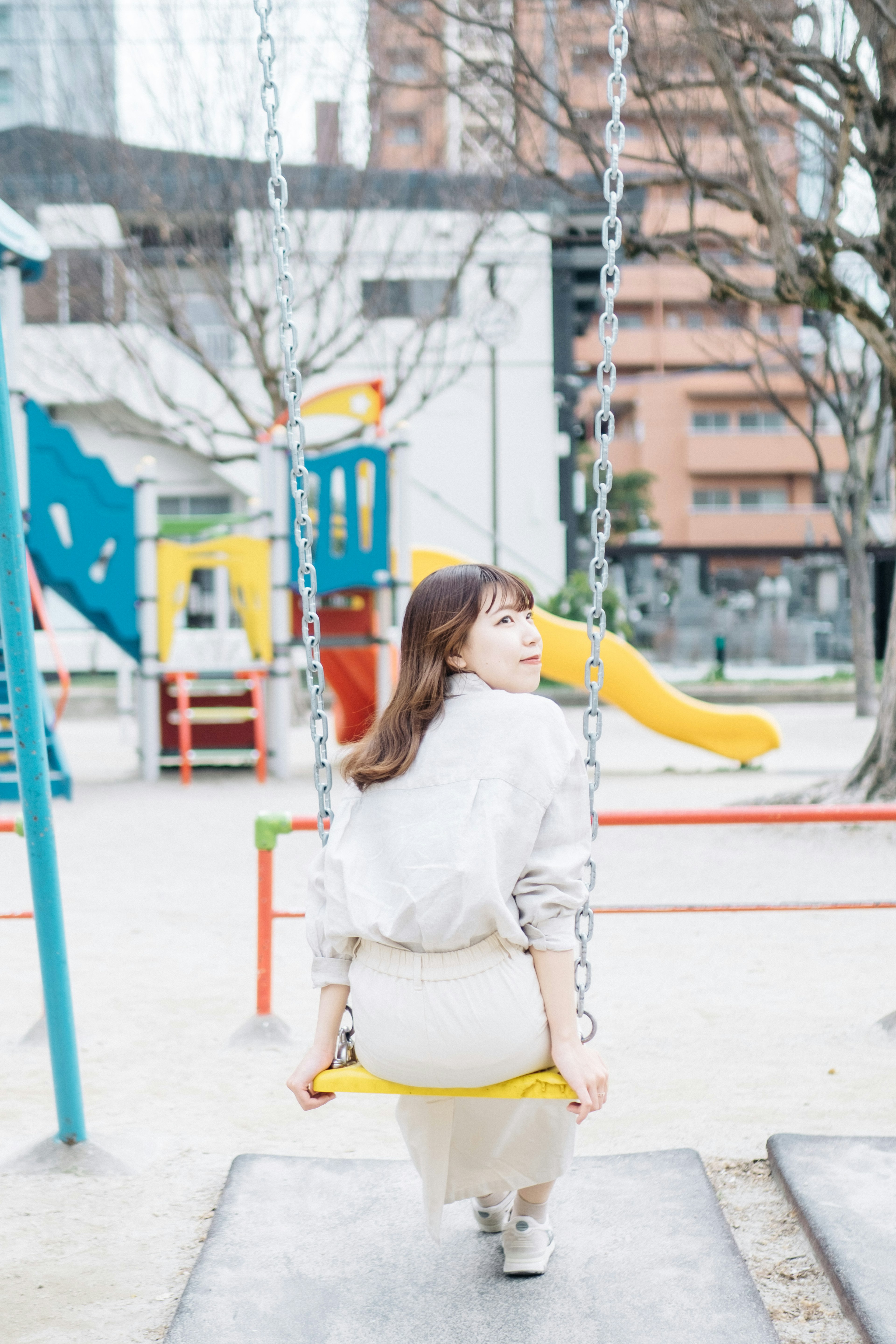 公園のブランコに座る女性の後ろ姿とカラフルな遊具