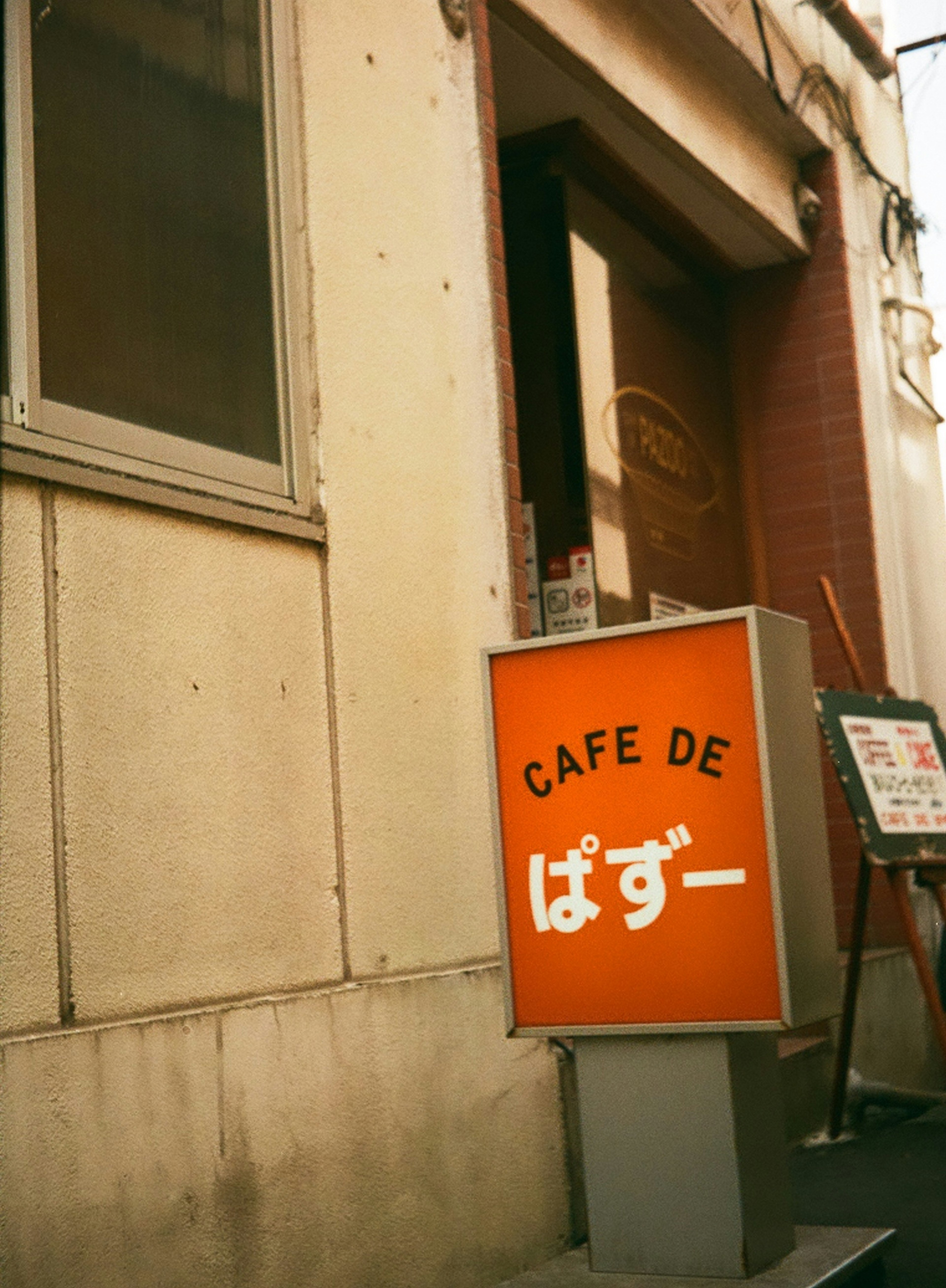 Cafeeingang mit einem orangefarbenen Schild mit der Aufschrift CAFE DE ぱずー